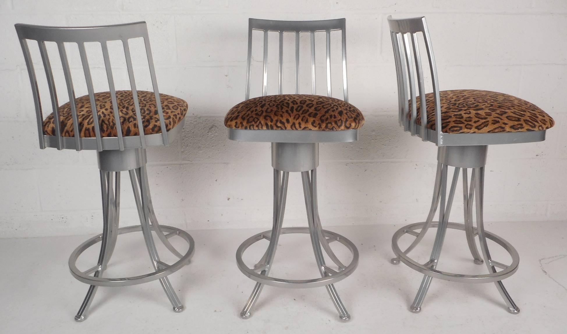This gorgeous Mid-Century Modern style set of three bar stools feature a unique slatted backrest with stylish curved legs. Sleek design with plush velvet leopard upholstery and a circular kick rest placed perfectly for comfort. This unique set have