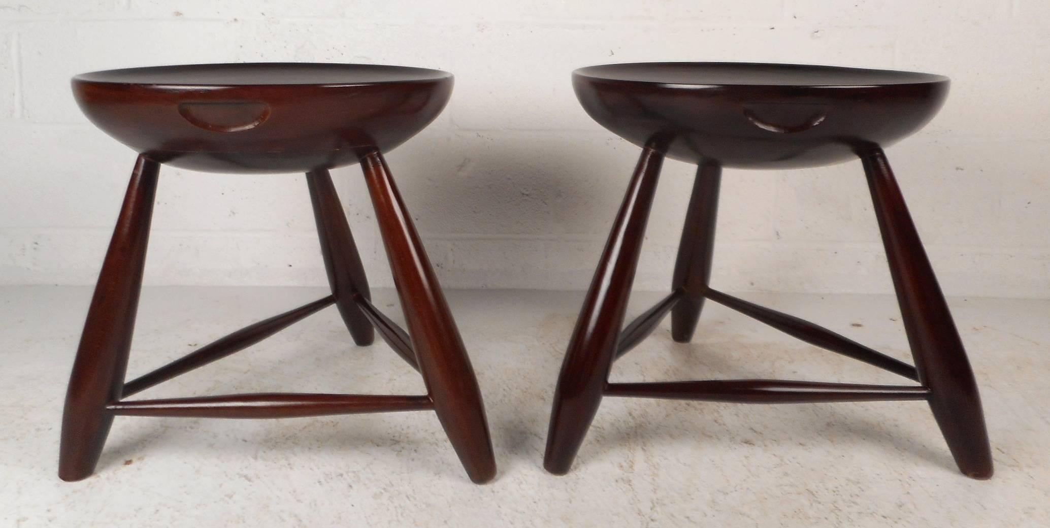 This stunning pair of vintage modern end tables feature unique round tops with smooth raised edges. The unique design has three splayed legs tied together by stretchers ensuring sturdiness. Versatile design with gorgeous wood grain can be used as