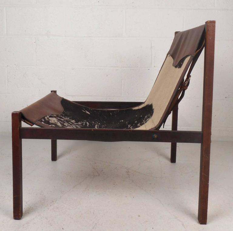 Elegant Mid-Century Modern lounge chair features a combination of cow hide and leather upholstery. Unusual stitched leather around each leg and thick leather belts easily support the weight from underneath. This rare chair is signed, 