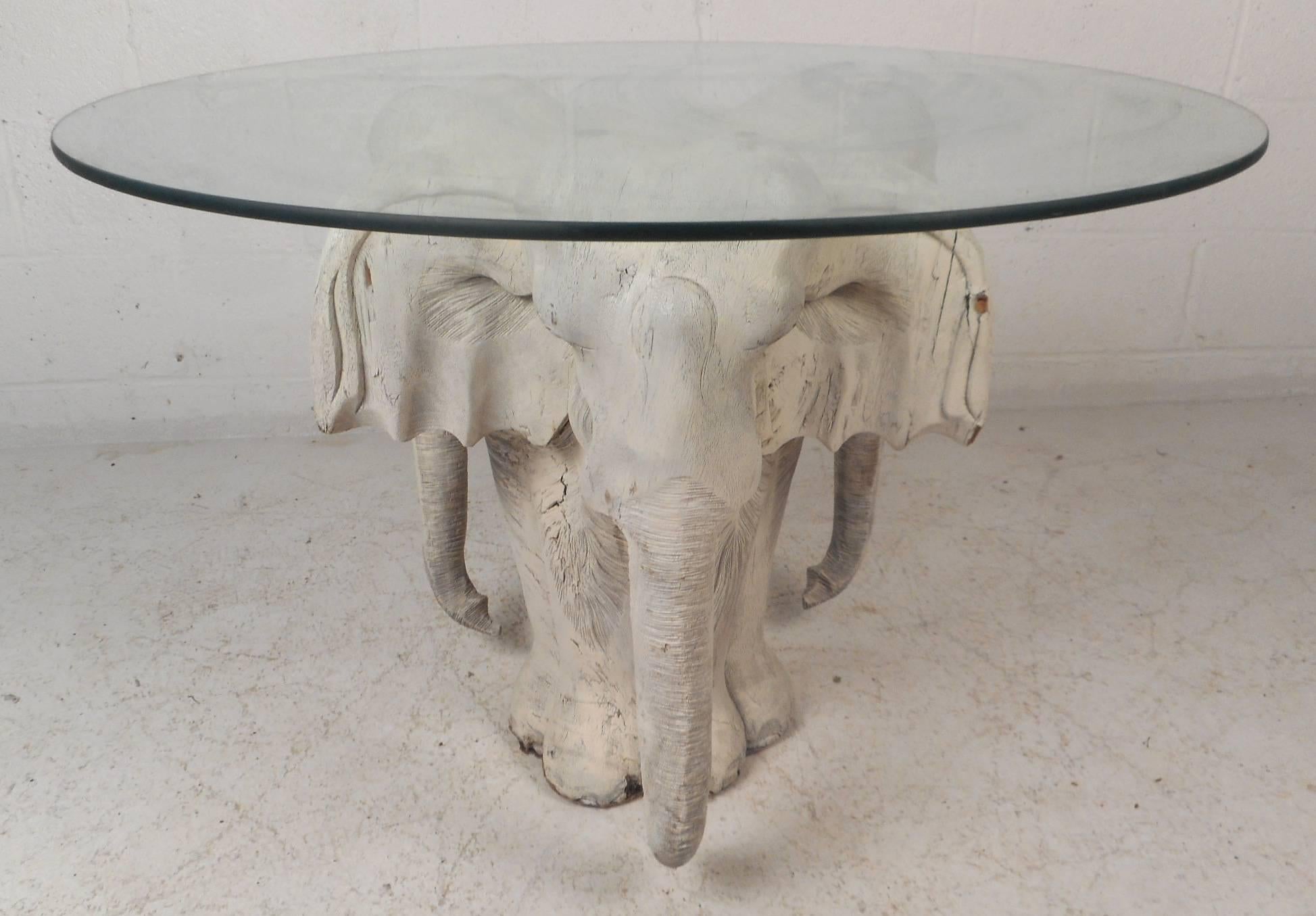 This beautiful vintage modern coffee table features a hand-carved wood base displaying an elephant on three sides. Unusual design with exquisite detail from the tusk to the ears. Sleek and Primitive piece has a round glass top with a tint of green.