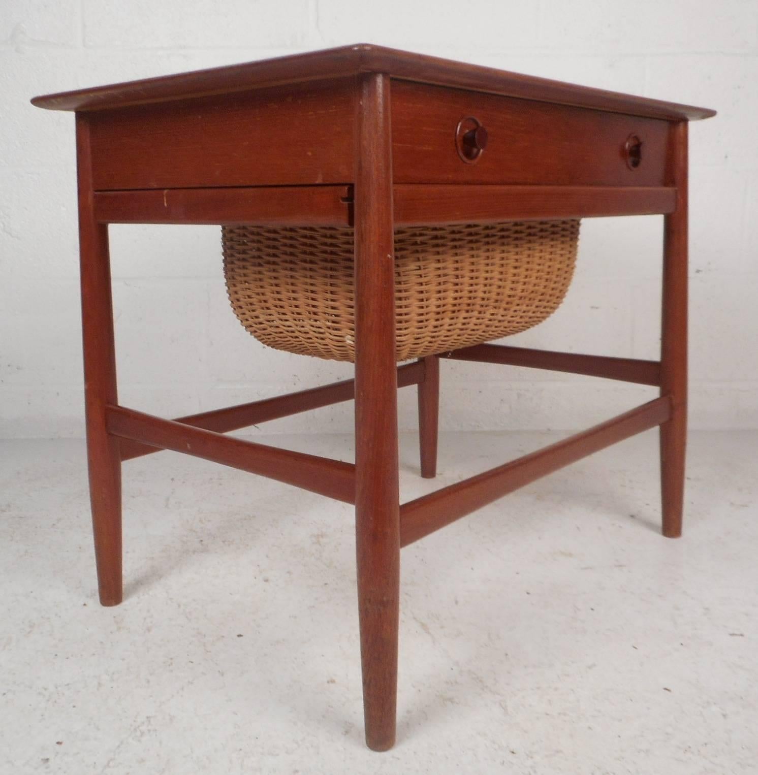 Stunning vintage modern side table features a pull-out woven basket and a large drawer with unique circular pulls. Sleek and sturdy design with stretchers in between each tapered leg. Beautiful teak wood grain and a finished back add to the allure.