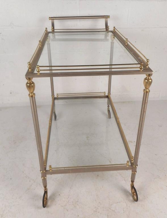 This gorgeous vintage modern serving cart features stylish sculpted brass fixtures and unique brass rods around each shelf. Sleek design offers plenty of room for items on its two glass shelves. This elegant mid-century piece has unusual brass