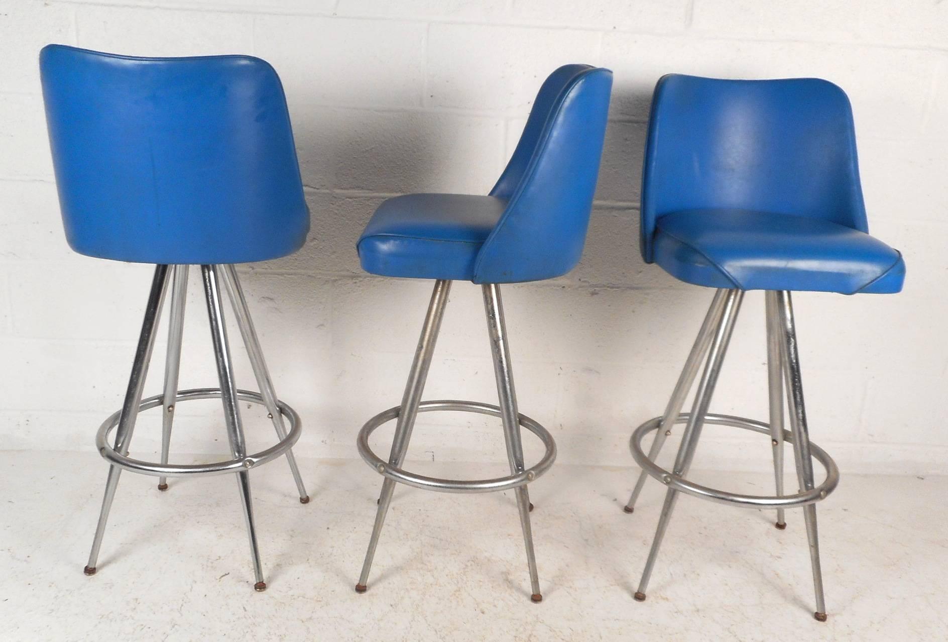 This beautiful set of four vintage modern bar stools feature elegant royal blue vinyl seats with the ability to swivel. Stylish design has tapered chrome rod legs that splay outward with a convenient round kick rest. Comfortable and sturdy chairs