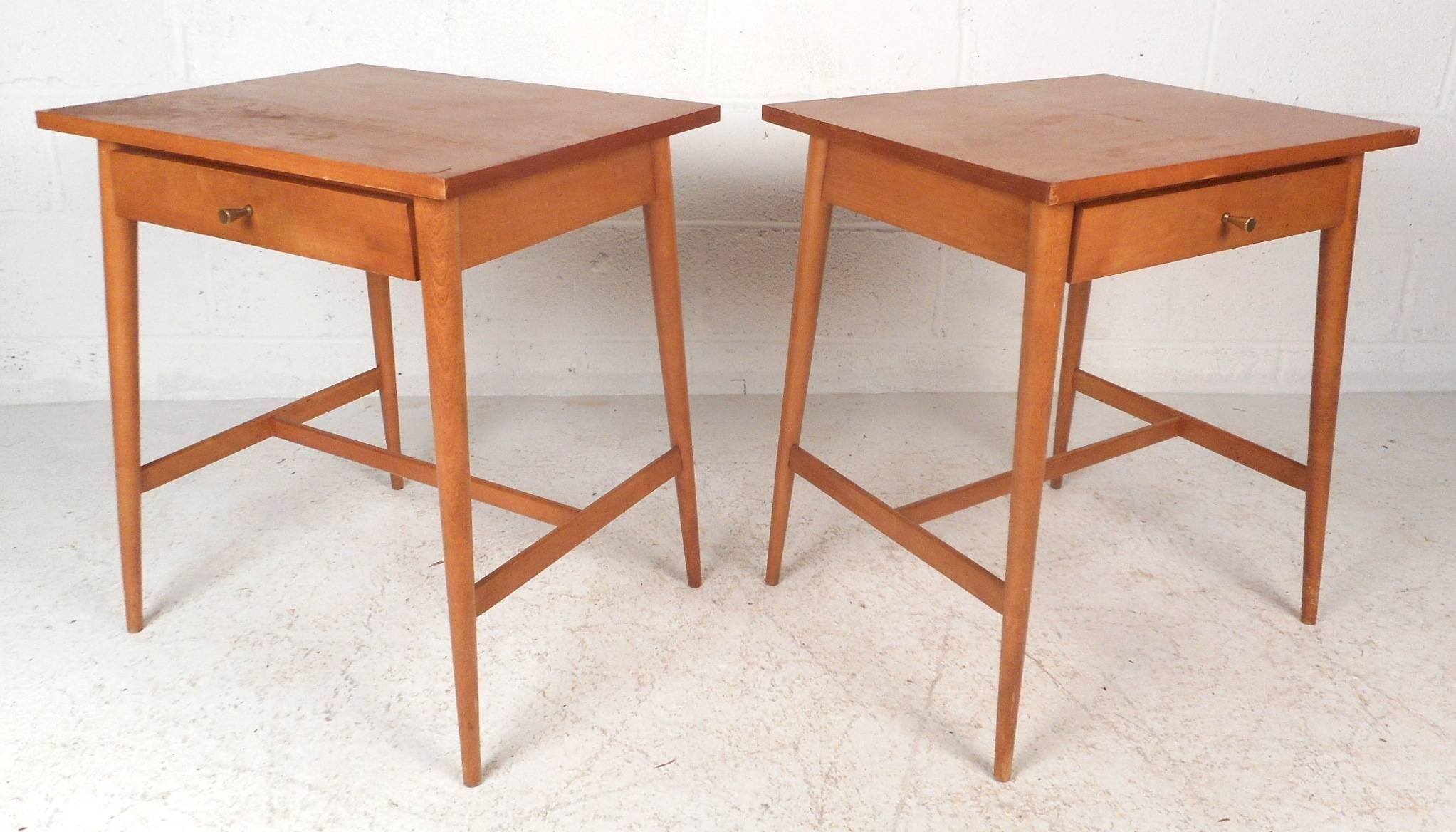 Beautiful pair of Mid-Century Modern nightstands with a vintage blonde maple finish. This stylish piece features one drawer with a unique conical brass pull. Sleek design with an oversized top and splayed tapered legs with stretchers for added