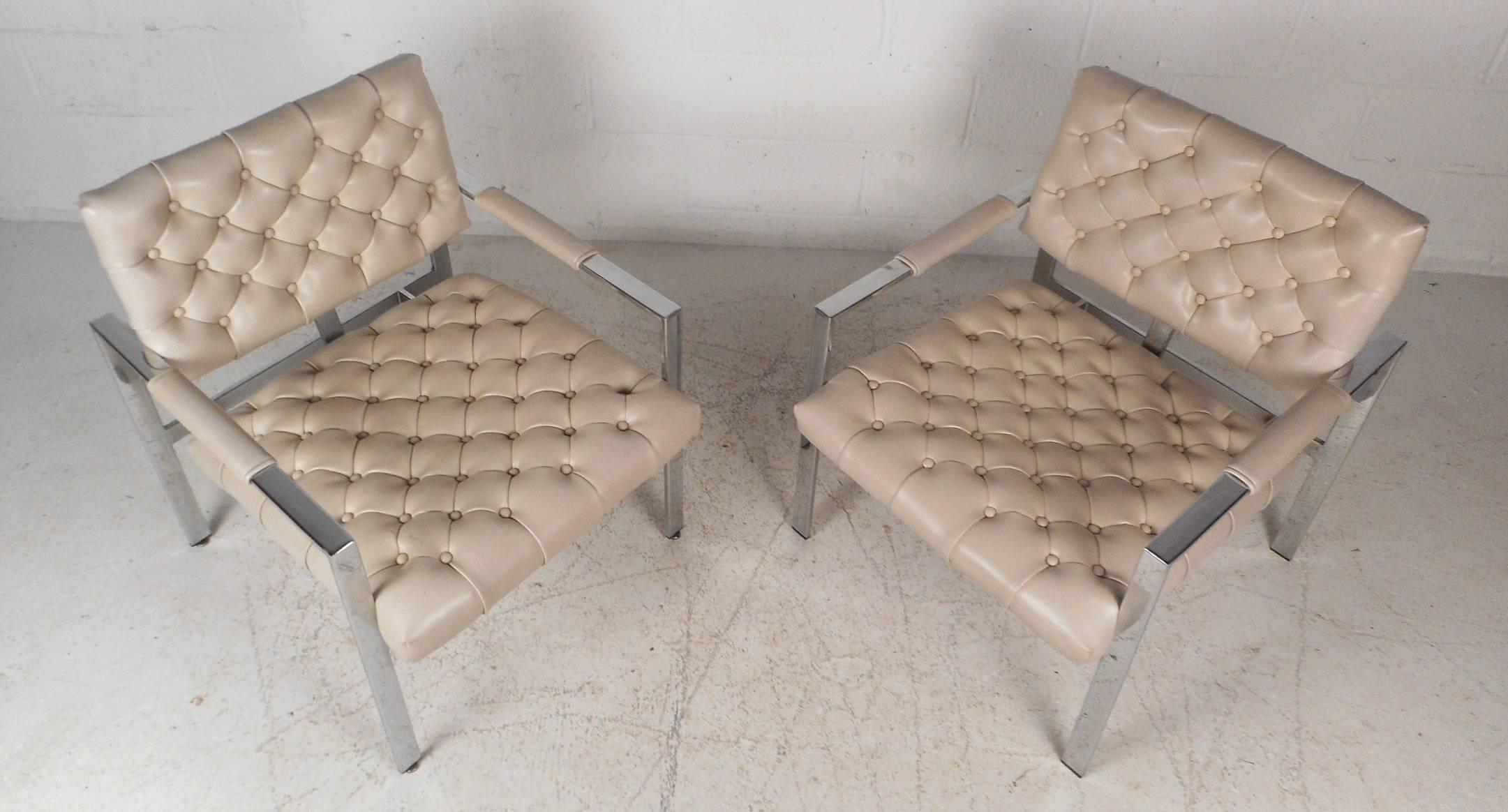 This gorgeous pair of vintage modern lounge chairs feature a heavy flat bar chrome frame with off-white tufted vinyl upholstery. The sleek design ensures comfort with padded arm rests and a floating style backrest. These wide Mid-Century armchairs