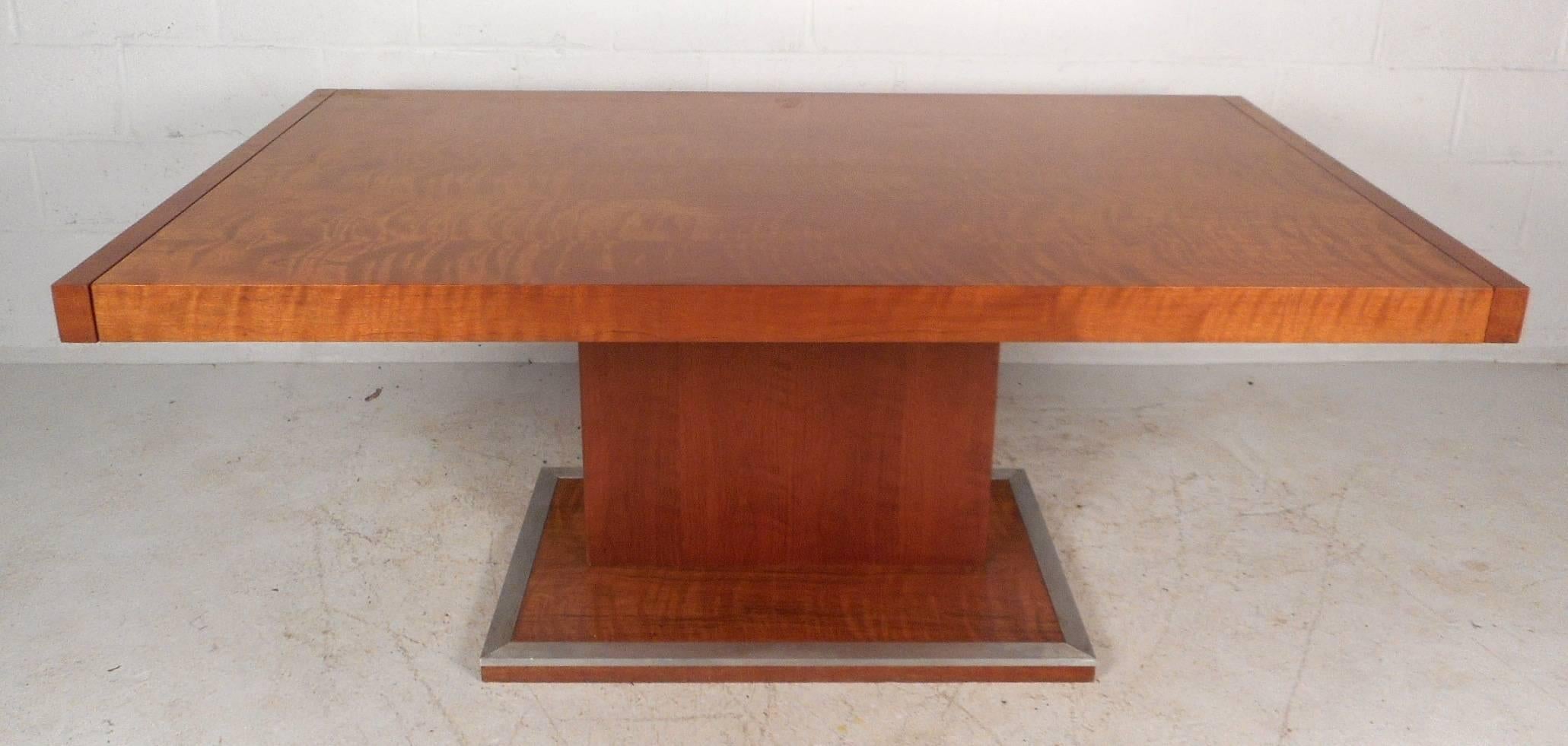 This beautiful vintage modern dining table is made of burl maple wood and includes two leaves that easily insert on each end. Unique floating top design with a stylish and sturdy pedestal style base outlined in metal trim. Impressive piece goes from