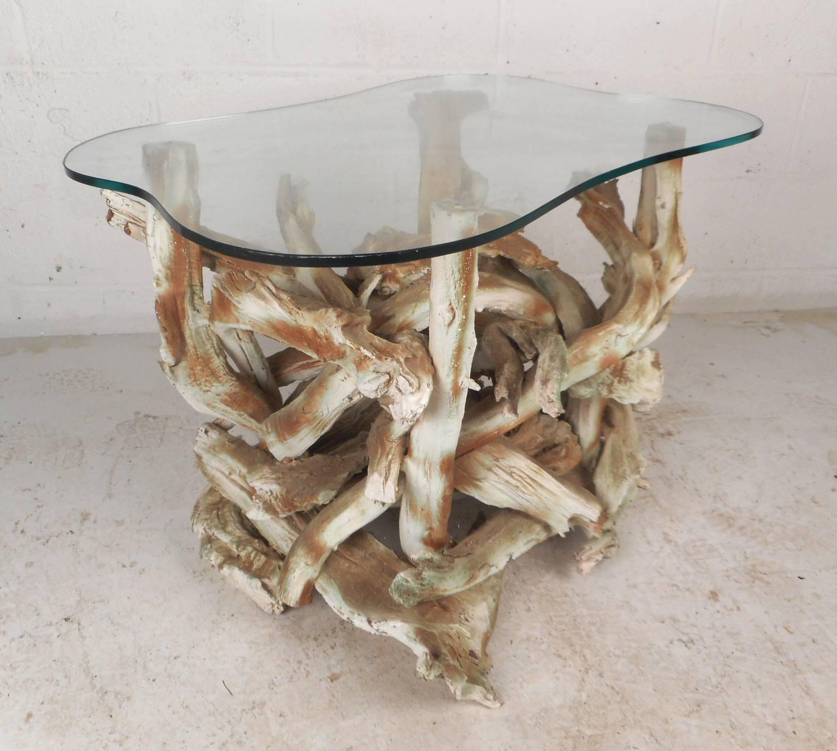 Cette superbe table d'appoint vintage moderne présente une base unique en bois flotté et un plateau en verre épais en forme d'amibe. Un design fascinant avec des détails complexes et de légères teintes de vert sur la base. Cette table d'appoint