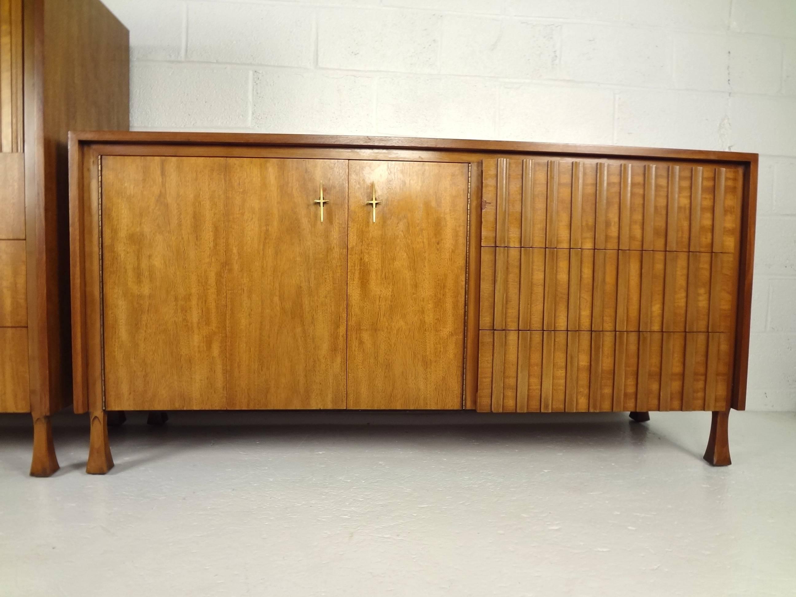 This handsome vintage modern bedroom set includes a high boy and a low dresser with unusual louvered fronts. The high boy features a hidden storage compartment on the top hidden by tambour doors and three hefty drawers on the bottom. The low dresser