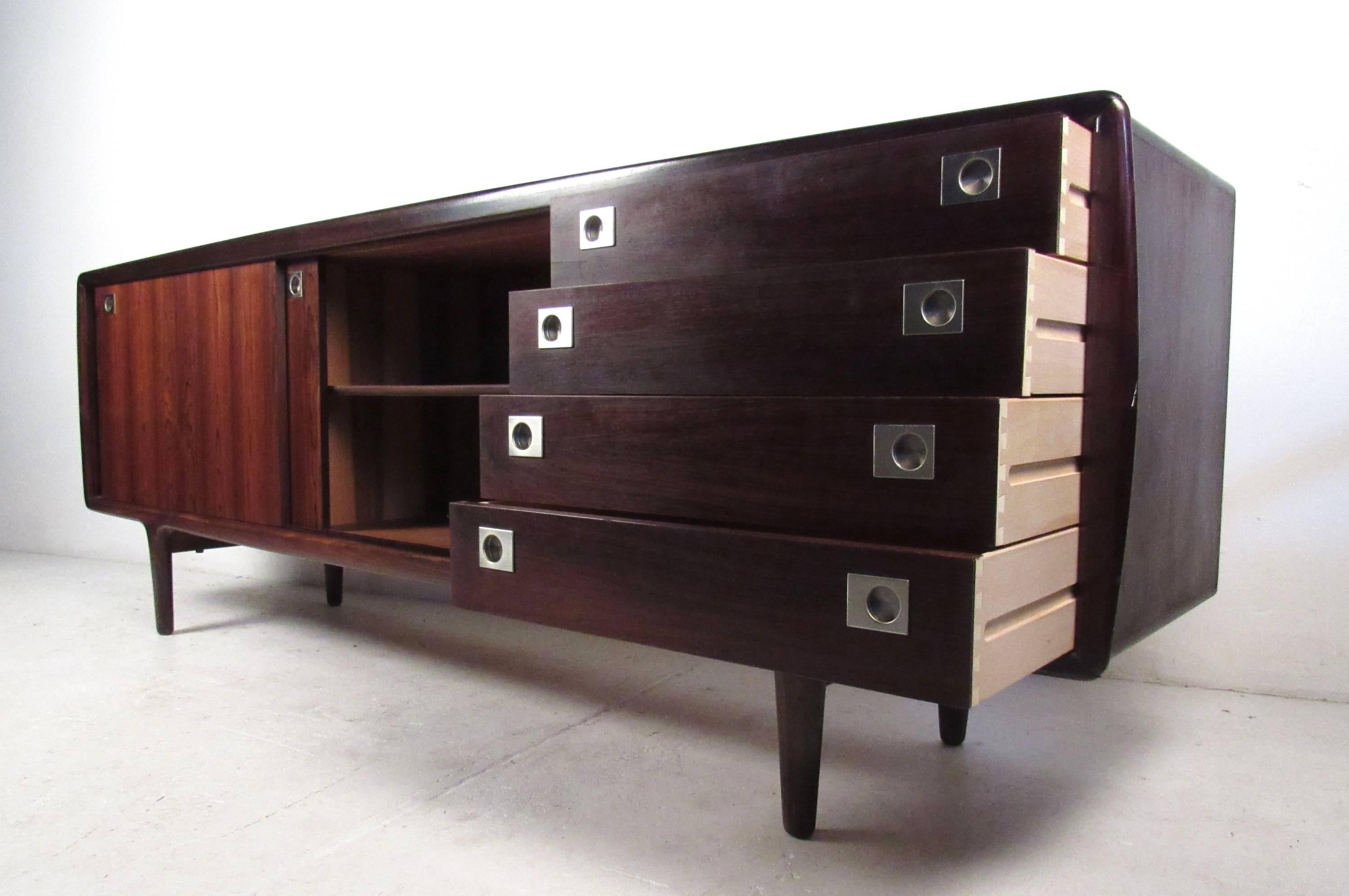 This stunning long vintage modern sideboard features unique recessed chrome pulls and sculpted tapered legs. Sleek Danish design by H.P. Hansen with elegant rosewood grain and clean lines. Four large drawers and two large compartments are hidden by