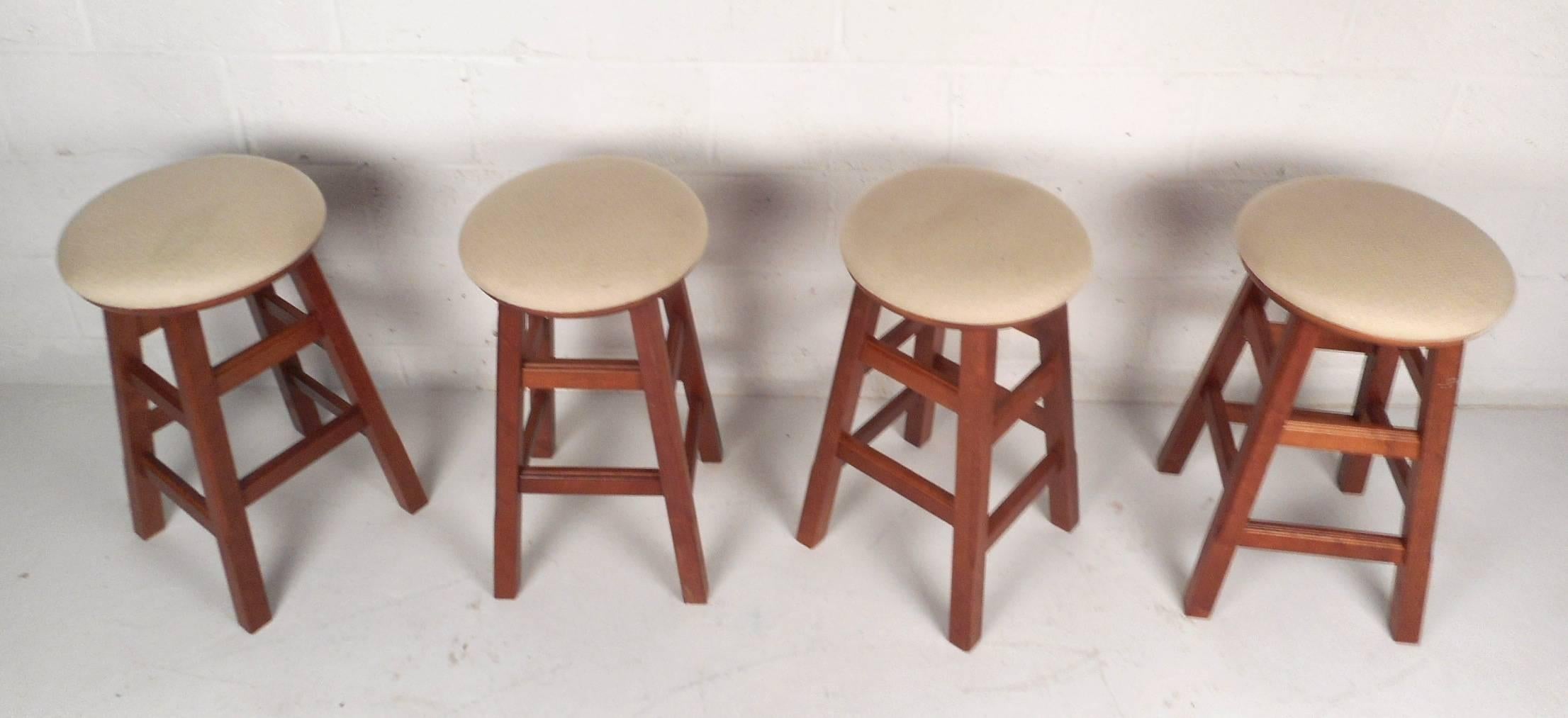 This beautiful set of four Mid-Century Modern style stools feature unique rotating seats with lovely white upholstery. This stylish set have sturdy wood frames with multiple stretchers that function as kick rests. Unusual design has a hidden ability