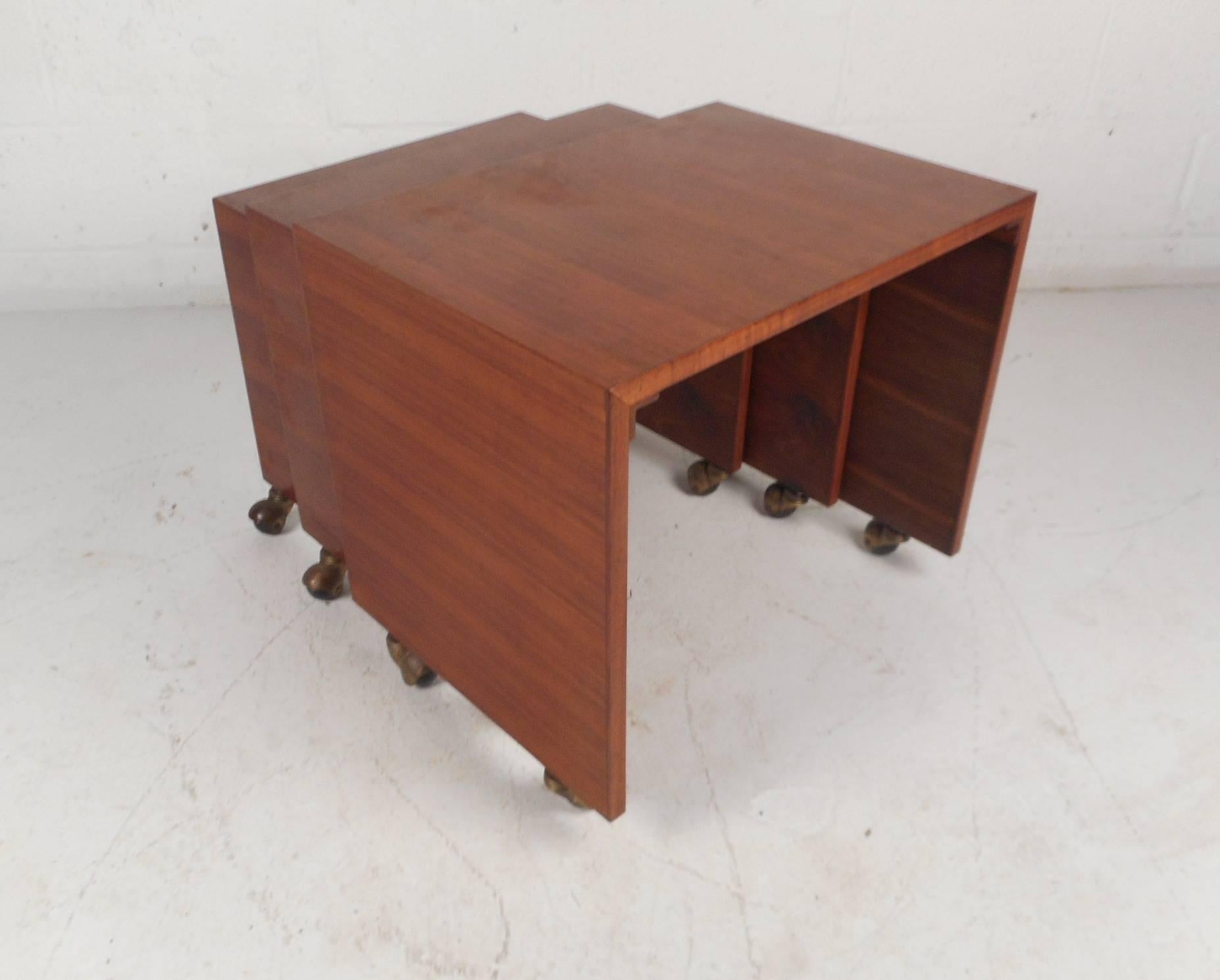 This beautiful vintage modern set of three nesting tables feature elegant walnut wood grain and a waterfall style shape. This heavy and solid set have castors providing added convenience. These unique Mid-Century pieces slide comfortably on top of