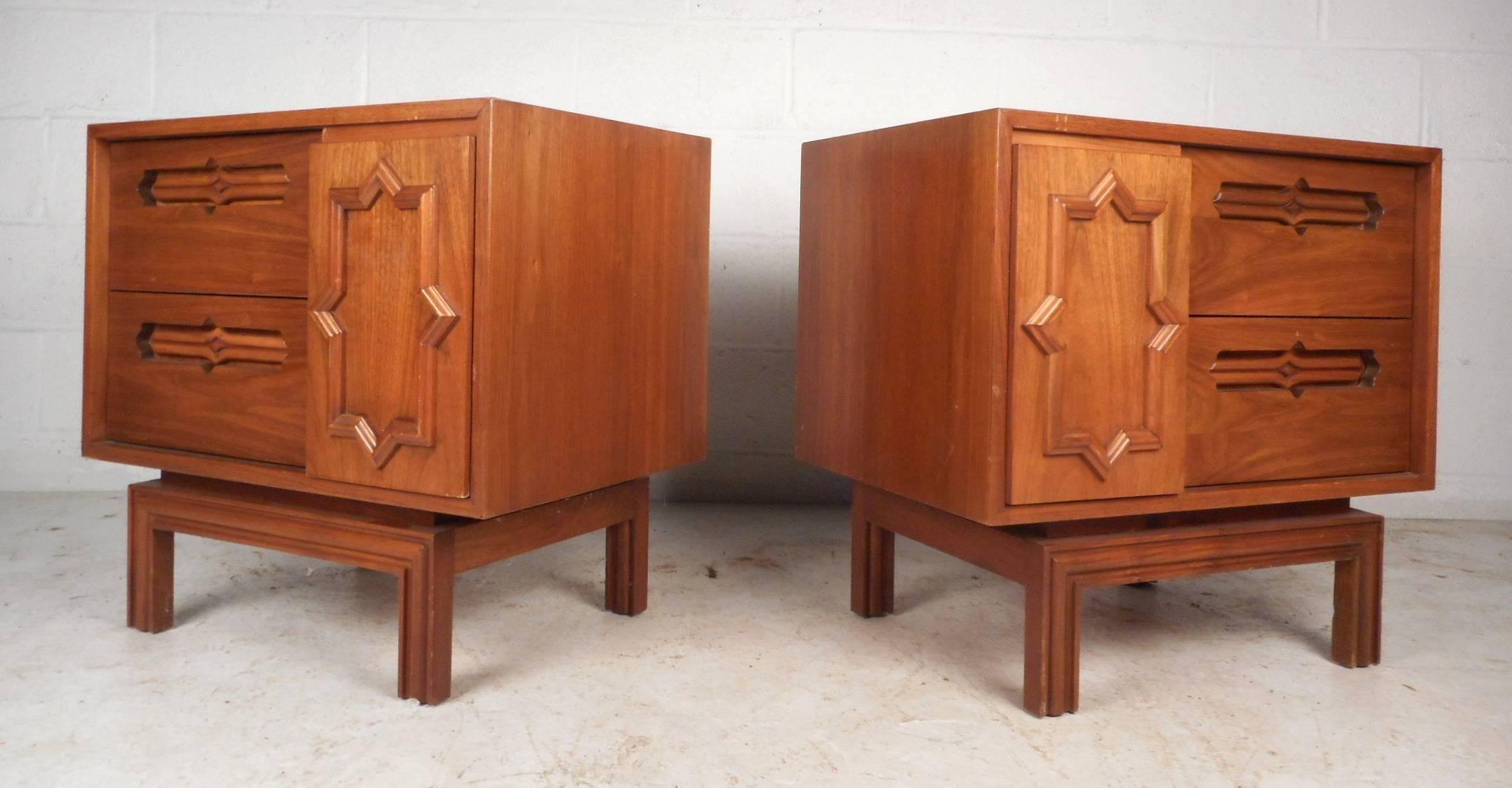 This stunning pair of vintage modern nightstands feature a unique front with carved designs and pulls. Unusual design with two drawers and a sliding door with a hidden compartment behind it. This one of a kind pair have a stylish base with etched