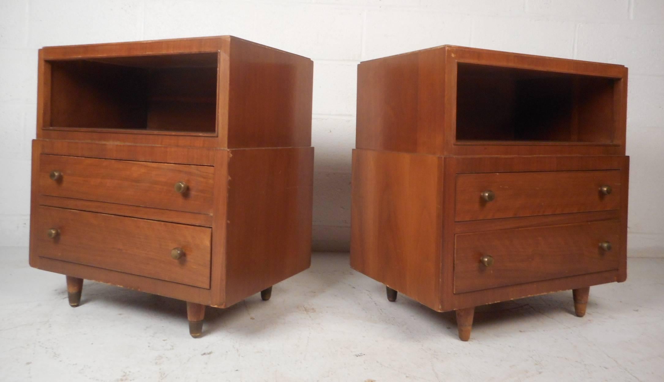 Stunning pair of Mid-Century Modern end tables by John Stuart with a vintage walnut finish and round brass drawer pulls. Stylish design features a compartment for storage on the top and two drawers on the bottom. These unique pieces have brass