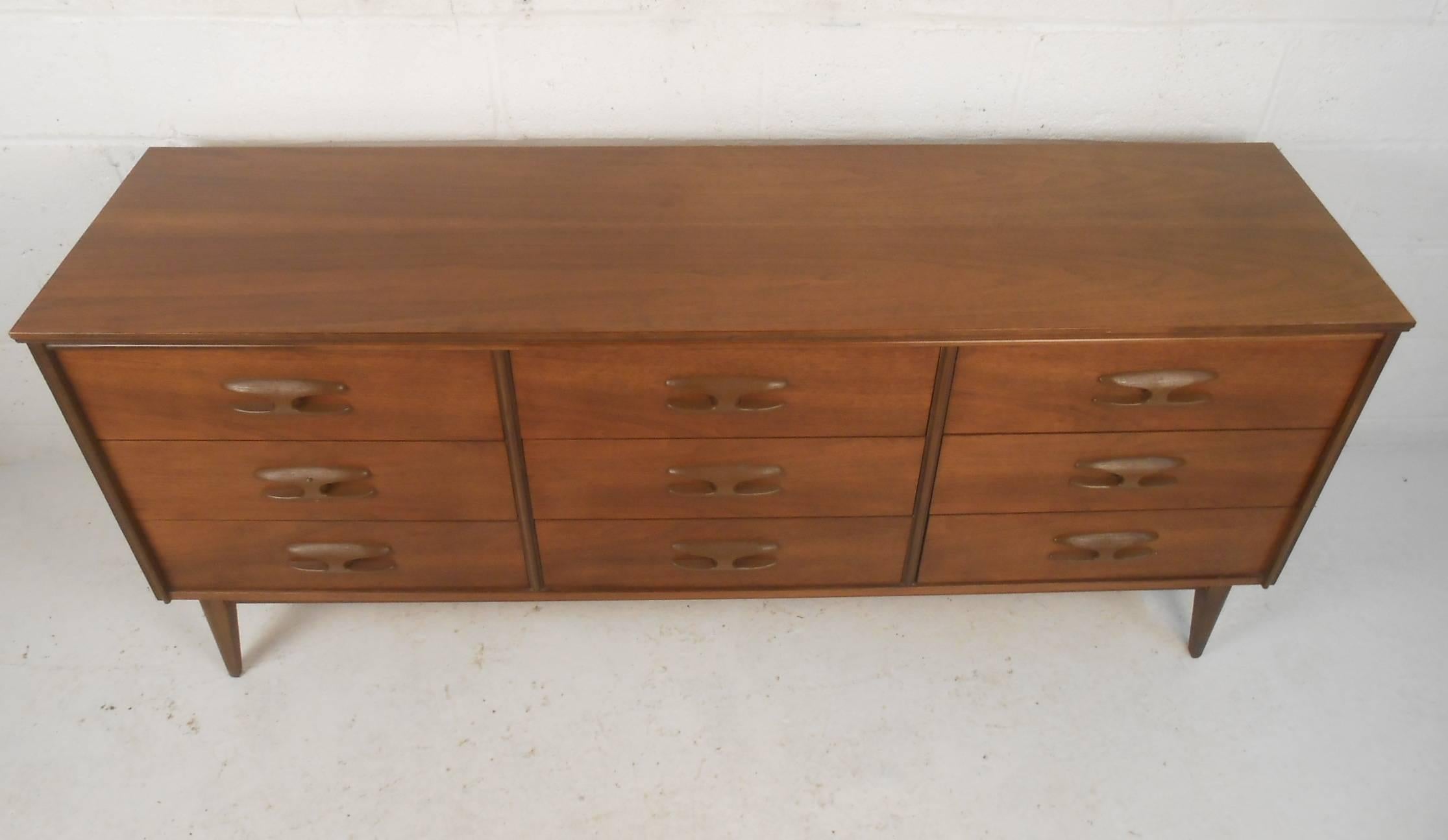 This beautiful vintage modern dresser features unusual sculpted pulls on each of its nine hefty drawers. This unique case piece provides plenty of room for storage without sacrificing style. The lovely dark walnut wood grain and splayed legs add to