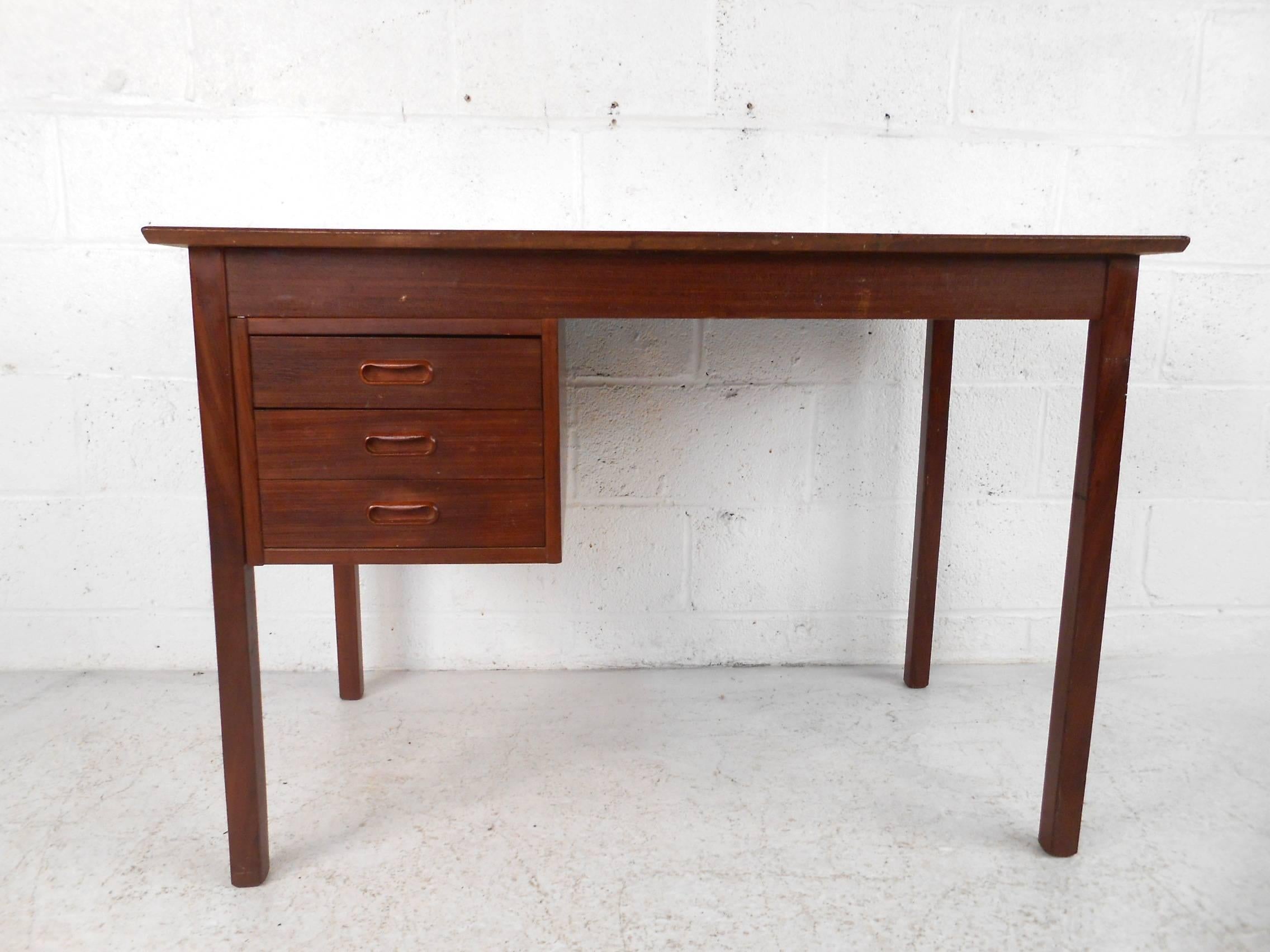 This beautiful vintage modern desk features three drawers with unique carved pulls. Wonderful compact design with an abundance of work space on the top and plenty of room for storage within its drawers. This sleek case piece has a finished back