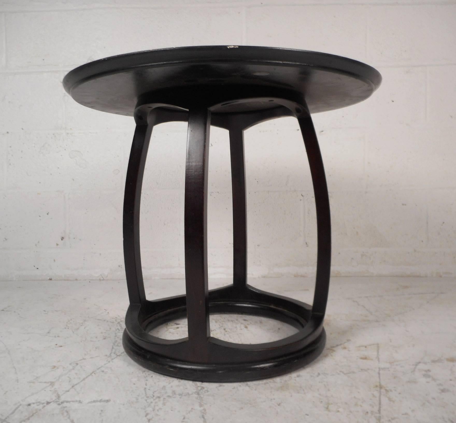 This beautiful vintage modern end table was designed by John Stuart. Sleek design has a round top with wood grain running in different directions. The unique ebonized frame features curved supports connecting to a sturdy open circular base. The