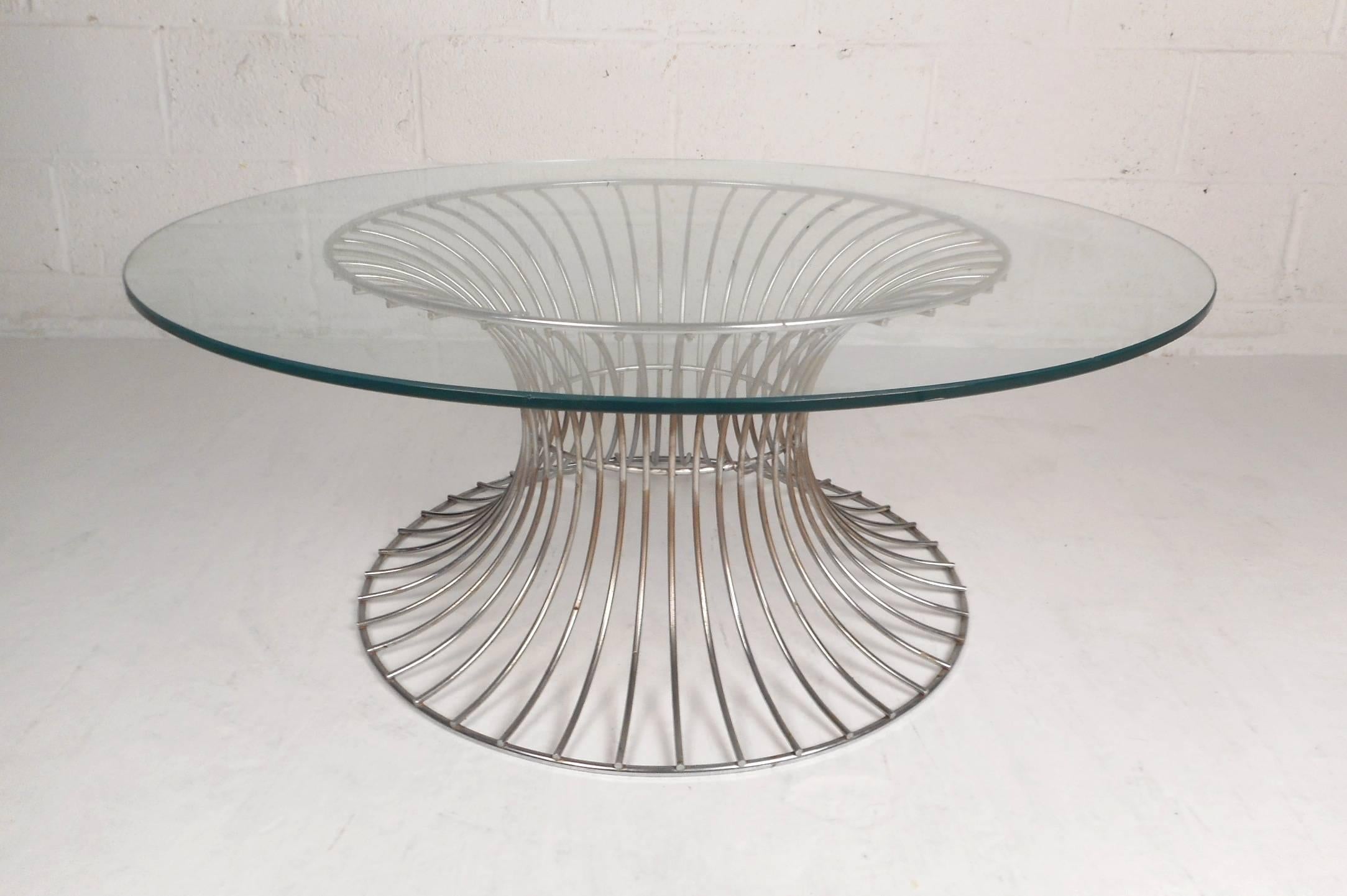 Cette magnifique table basse moderne vintage présente une base métallique à rayons et un plateau rond en verre. Le design unique en sablier sculpté assure la robustesse sans sacrifier le style. Cette table de cocktail aux lignes épurées est dotée