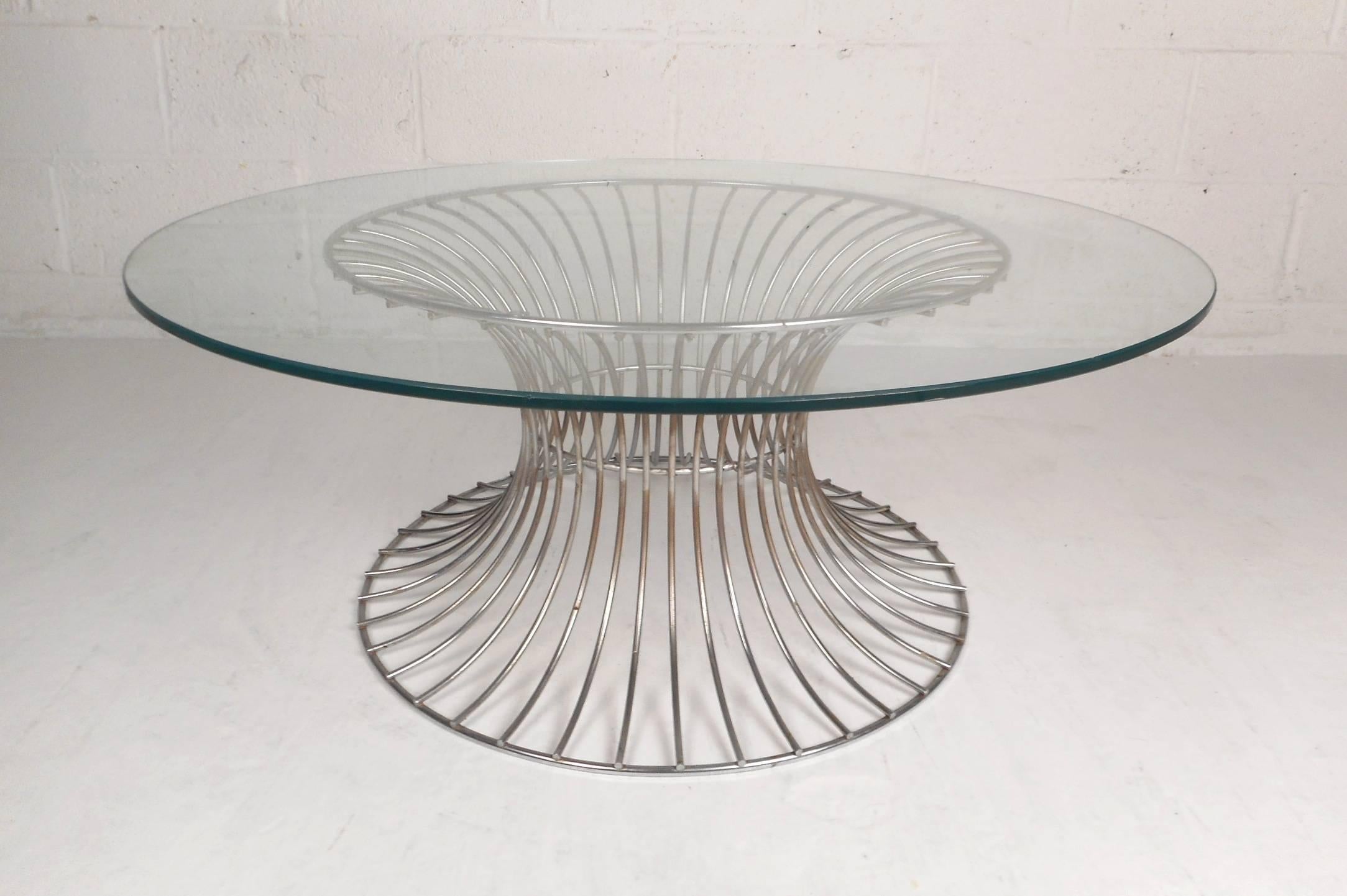 This beautiful vintage modern coffee table features a spoked metal base and a round glass top. The unique sculpted hourglass design ensures sturdiness without sacrificing style. This sleek cocktail table has an extremely thick glass top with a light