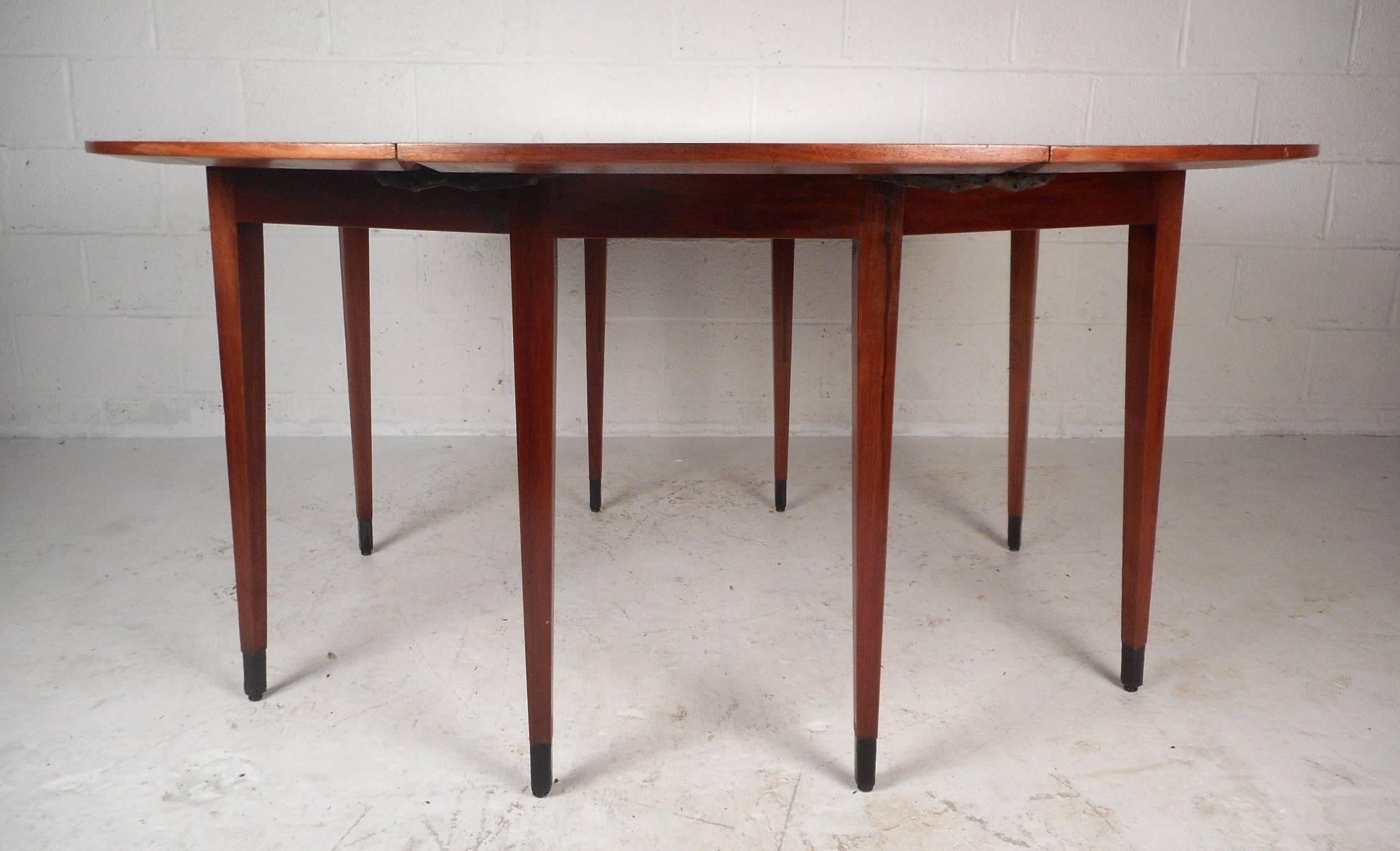 This gorgeous vintage modern dining table features a drop leaf design with gate legs. When this unique table is fully extended is measures at 72 inches wide by 60 inches deep. This newly refinished dining table has rich walnut wood grain throughout.