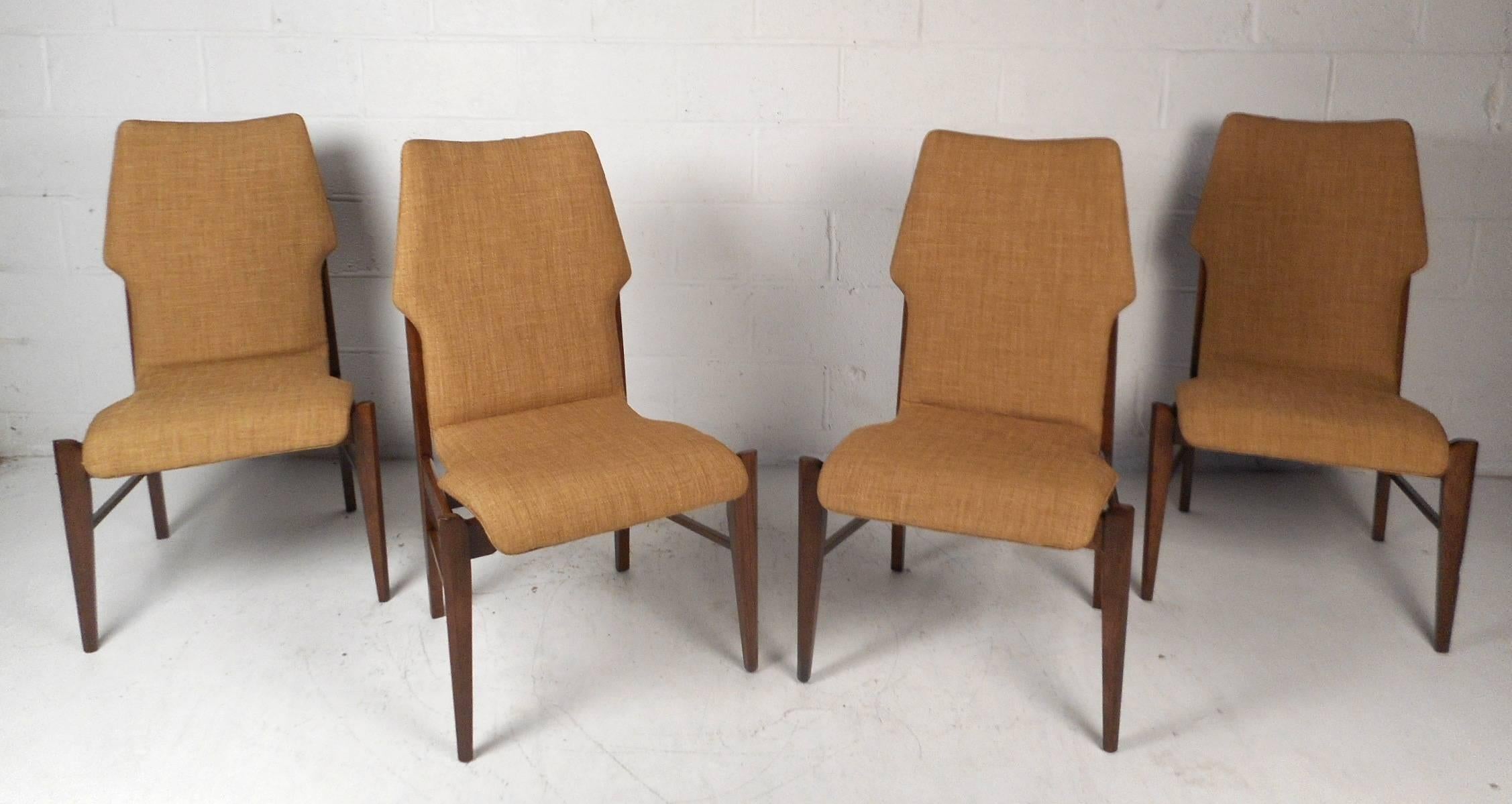 This gorgeous vintage modern set of four dining chairs feature unique walnut backs with upholstered seating. Sleek design with unique tapered legs and an unusually shaped back rest. Quality craftsmanship with elegant dark walnut wood grain and soft