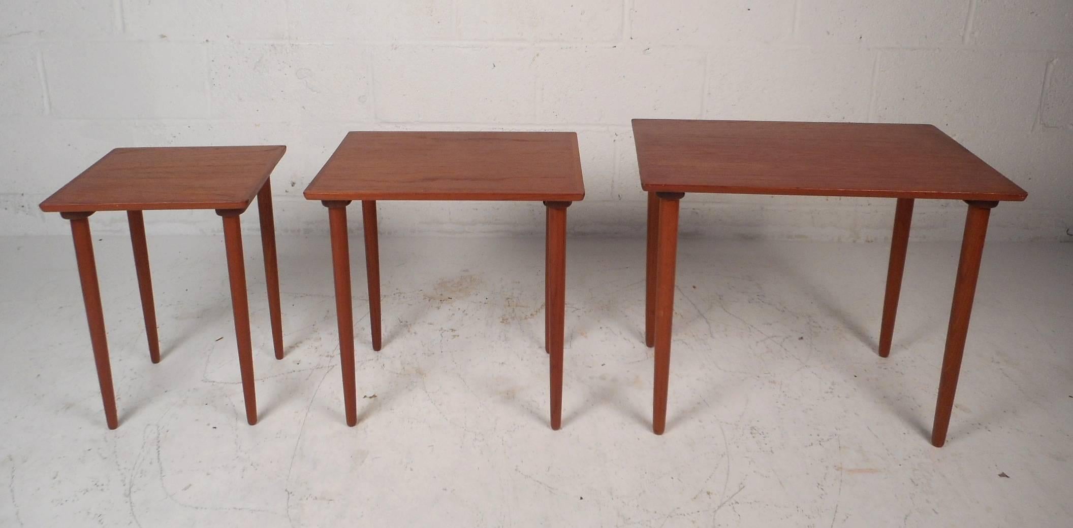 This gorgeous set of three vintage modern nesting tables feature long tapered legs and an elegant teak wood grain throughout. Sleek design allows each table to slide comfortably underneath each other for convenient storage. This wonderful Danish
