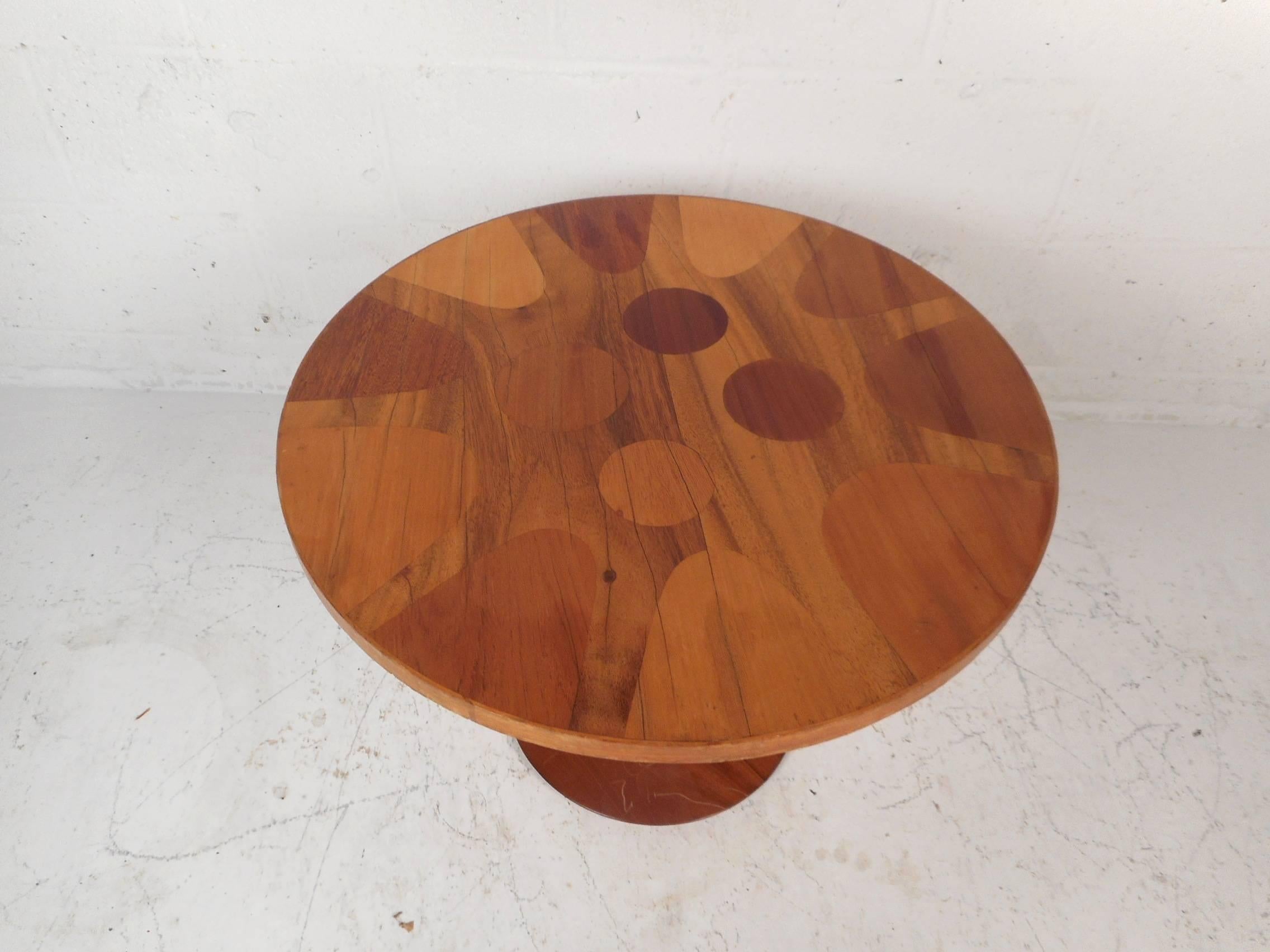 This wonderful vintage modern side table features a round top with unique inlays on a two-tone wood grain. The elegant tulip shape and sturdy round base add to the mid-century appeal. This unusual side table is sure to add style and grace to any