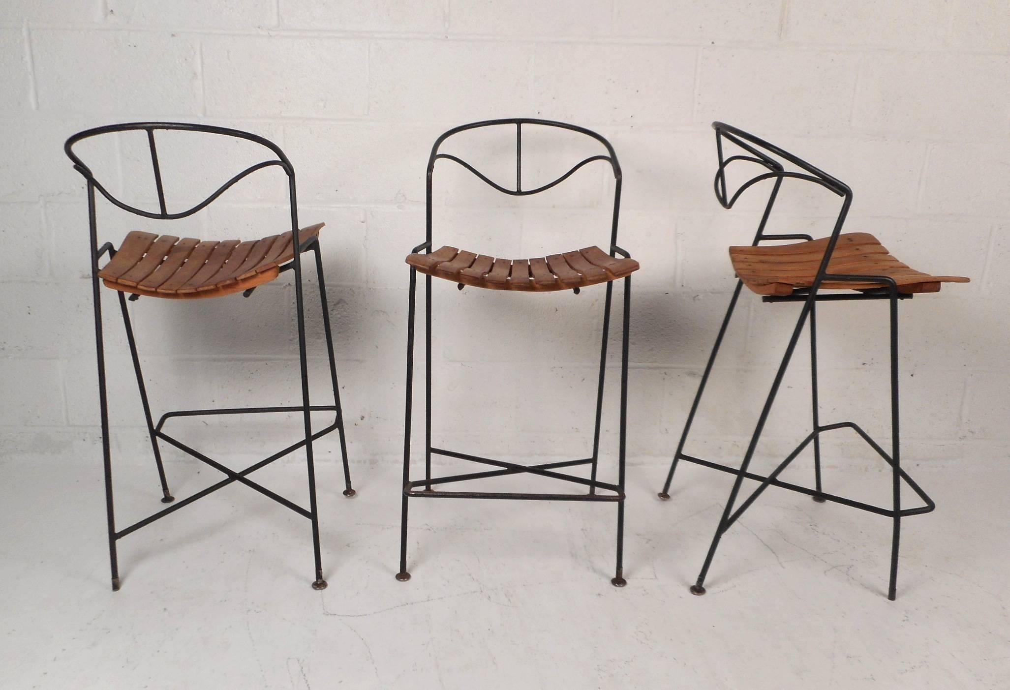 This beautiful set of three vintage modern bar stools feature a slatted seat and a sculpted wrought iron backrest. Fabulous design with an "X" base and a footrest for convenience and comfort. Unique stools with contoured seating and a