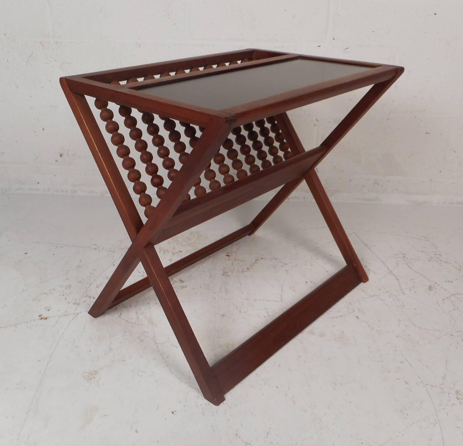 This gorgeous vintage modern magazine rack features a black laminate top allowing it to function as an end table. Unique Piece with a perforated design on one side and sturdy sled legs. This stylish and versatile mid-century piece has "X"