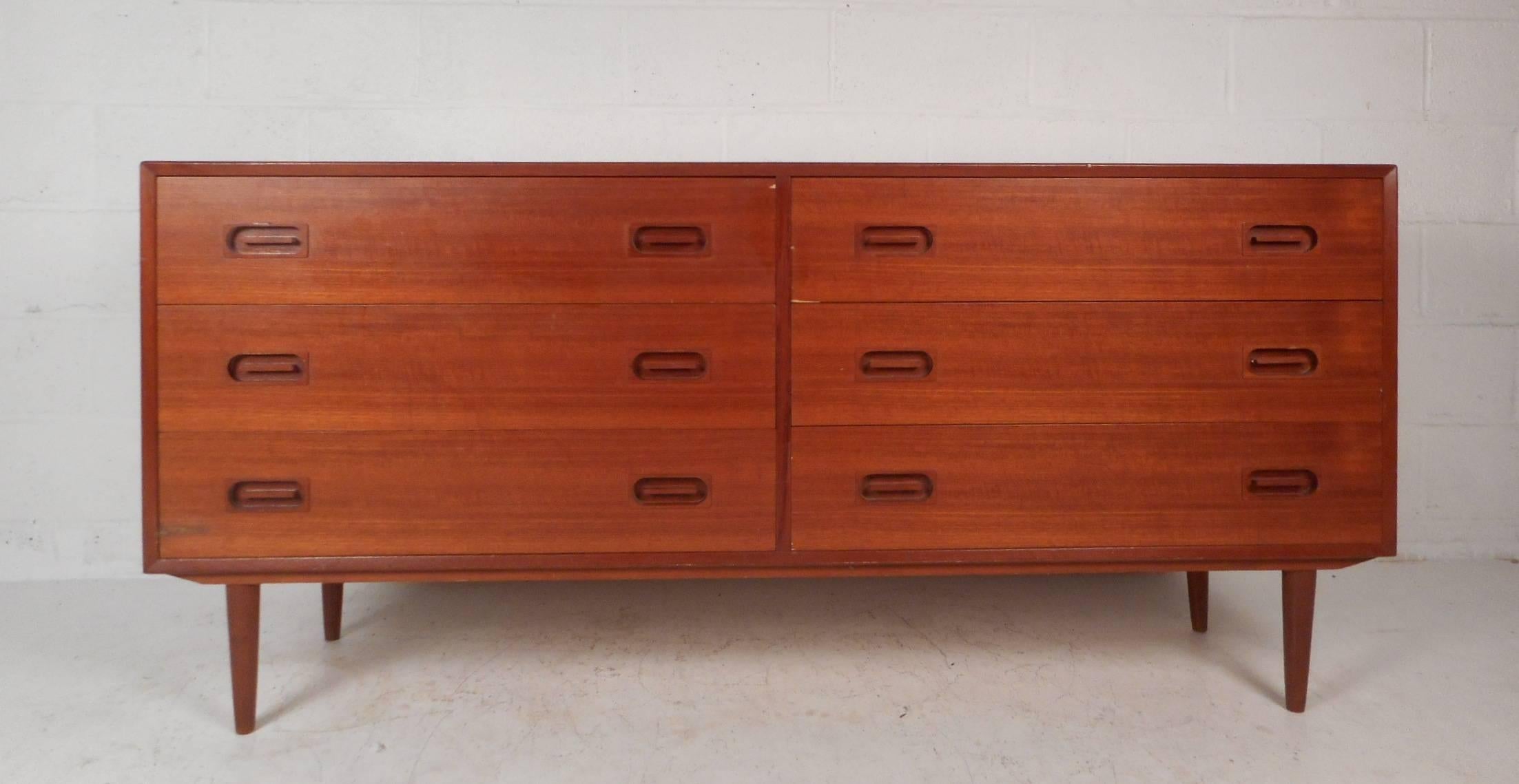 This gorgeous vintage modern dresser features six hefty drawers with unusual oval recessed pulls. Quality craftsmanship with elegant teak wood grain and tapered legs add to the midcentury appeal. This stunning case piece makes the perfect addition