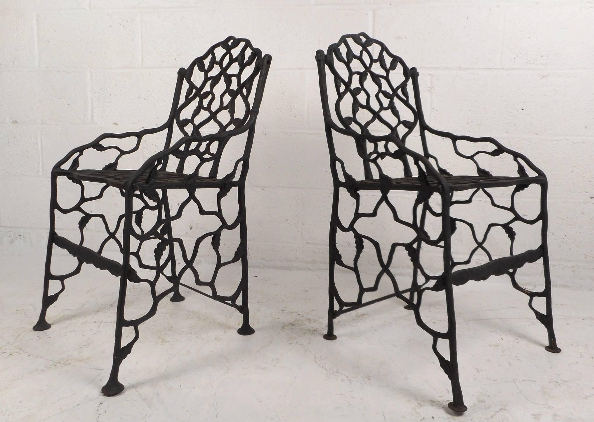 This beautiful pair of vintage cast iron garden chairs have a petite frame with bent iron and leaf detail throughout. Unusual design with a heavy iron frame, angled legs, and sculpted detail. This wonderful and rare pair of chairs make the perfect