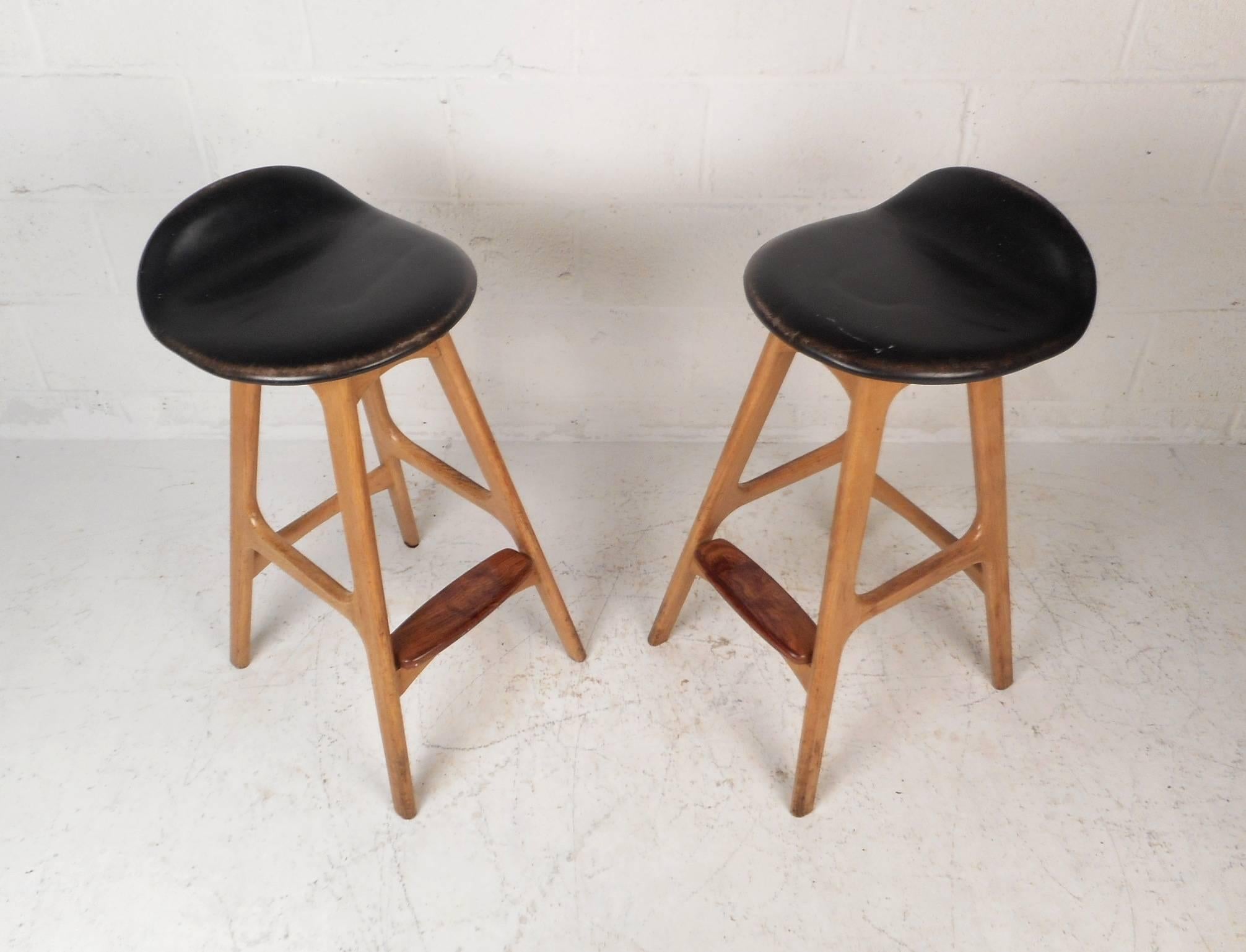 This beautiful pair of vintage modern bar stools feature leather seats and a solid teak frame. The unique sculpted seat has a raised back that functions as a partial backrest. Sleek design with angled legs, dove tail joints, and a conveniently