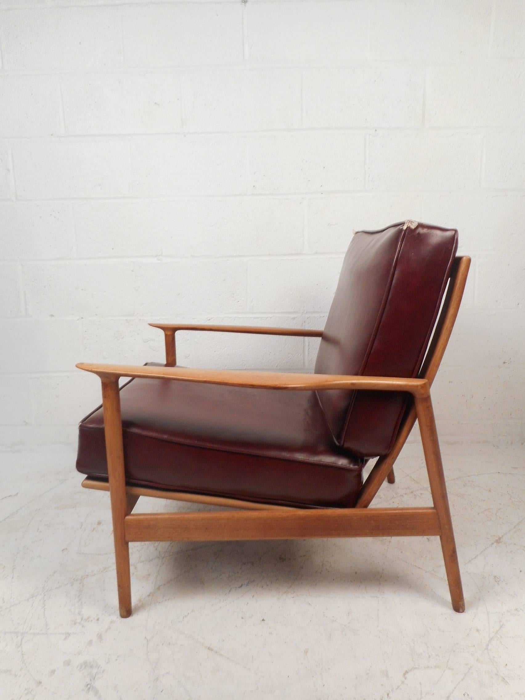 This gorgeous vintage modern lounge chair features a sculpted teak frame with thick padded vinyl cushions. Quality craftsmanship with angled legs, sculpted arm rests, and a unique carved slatted backrest. The thick padded cushions and angled design