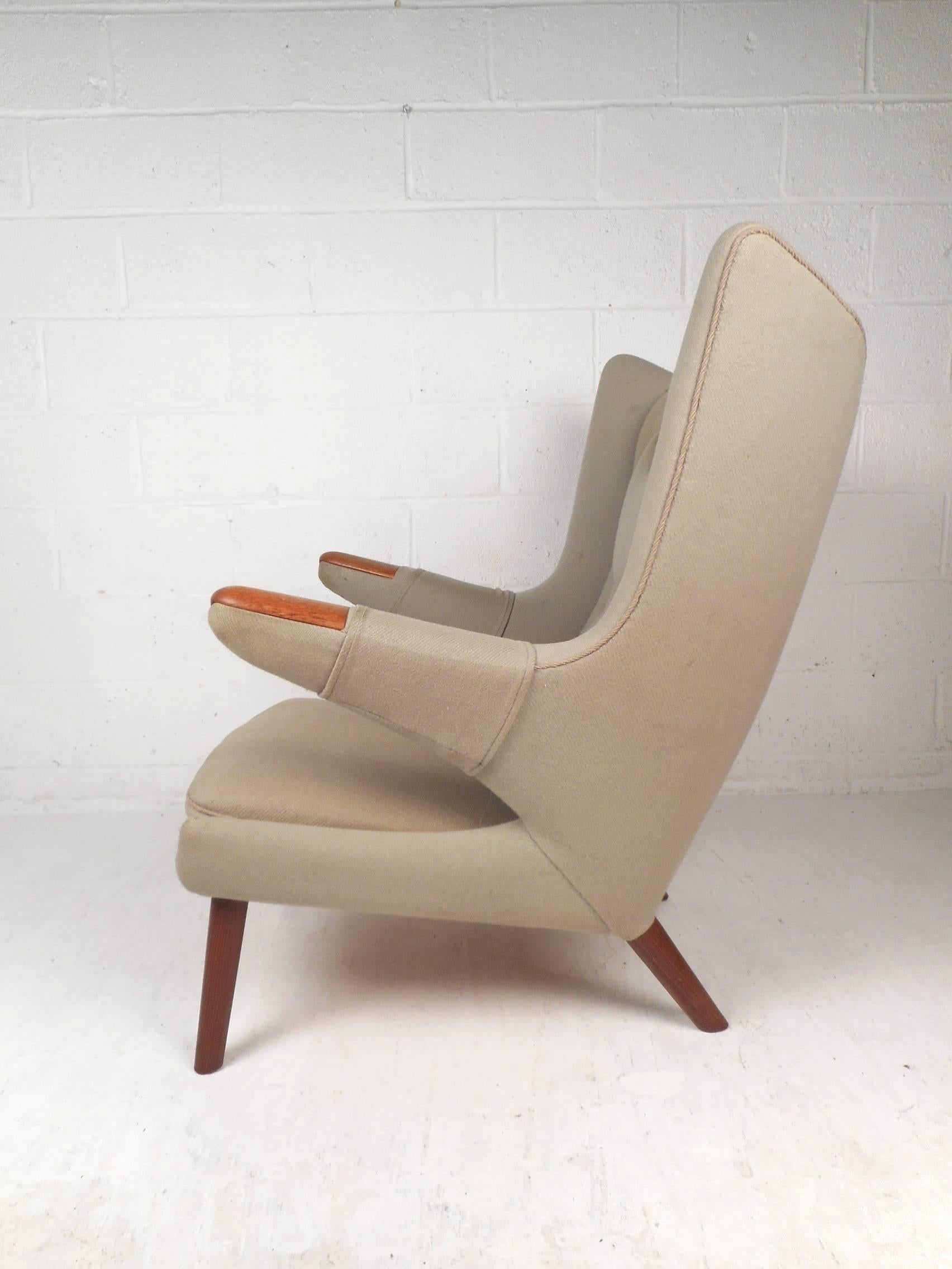 This beautiful vintage modern papa bear chair features a unique winged backrest and soft tufted upholstery. Sleek design with teak tipped armrests, splayed legs and thick padded seating. The stylish angled armrests and high backrest ensure optimal