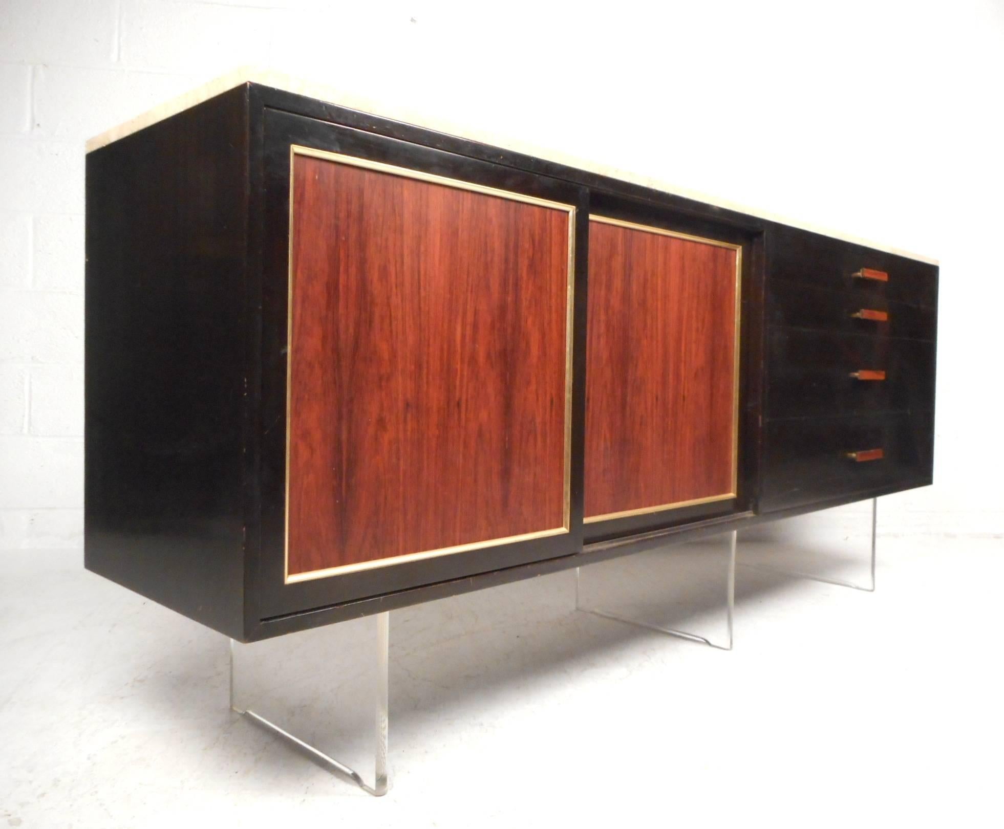 This handsome vintage modern sideboard features plenty of room for storage within its hefty drawers and large hidden compartment with a shelf. Sleek two-tone design with a sturdy Lucite base, unusual wood front drawer pulls, and an elegant ebonized