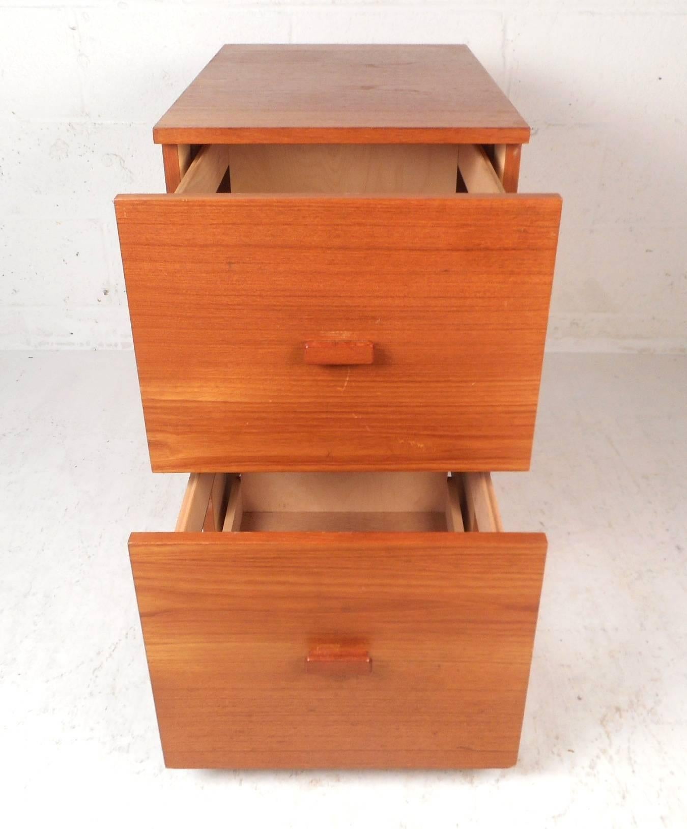 This wonderful vintage modern cabinet features two large drawers for storage. Stylish design with sculpted drawer pulls, a finished back, and four wheels underneath for convenience. Quality construction with elegant teak wood grain throughout. This