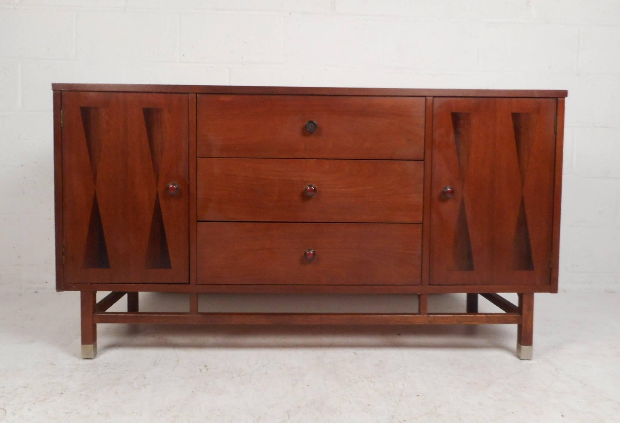 Wonderful vintage modern walnut sideboard with three hefty drawers in the centre and two large compartments on each side hidden by cabinet doors. The sleek design has unique dark colored inlays on the front of each door and stylish circular pulls on