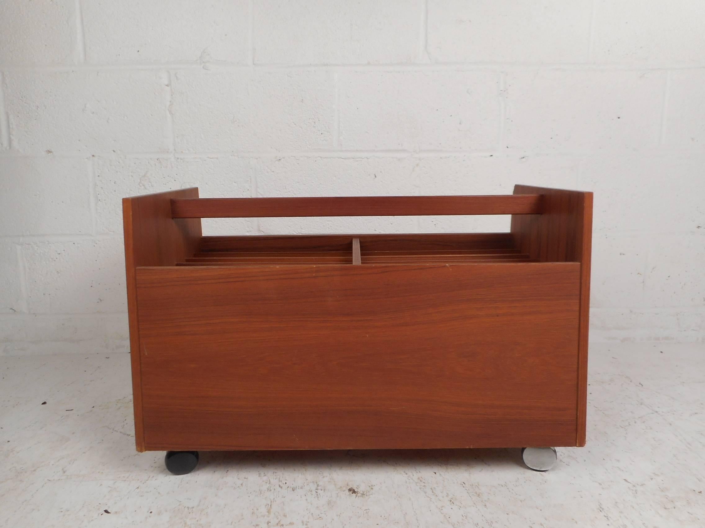 This gorgeous vintage modern magazine rack sits on top of four castors and has plenty of space within to store items. Stylish design with a convenient handle and elegant teak wood grain. This fabulous mid-century piece makes the perfect addition to