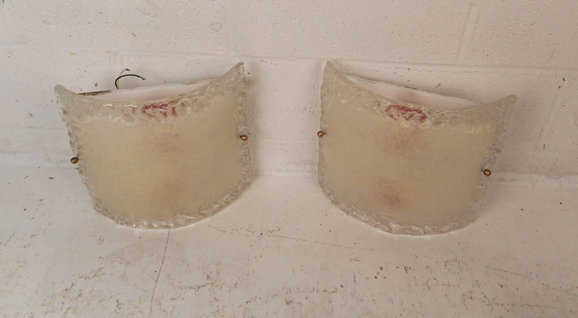 This elegant pair of Mid-Century Modern wall sconces feature thick textured glass fronts and a fixture with two sockets behind it. This stunning Murano style pair of lamps make the perfect eye catching addition to any modern interior. Please confirm