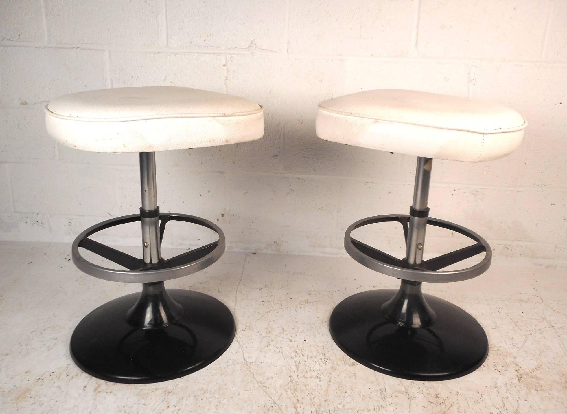 This beautiful pair of vintage modern swivel bar stools feature thick padded seats covered in white vinyl. Sleek design with a black metal base and a convenient circular foot rest. This comfortable pair of mid-century stools make the perfect