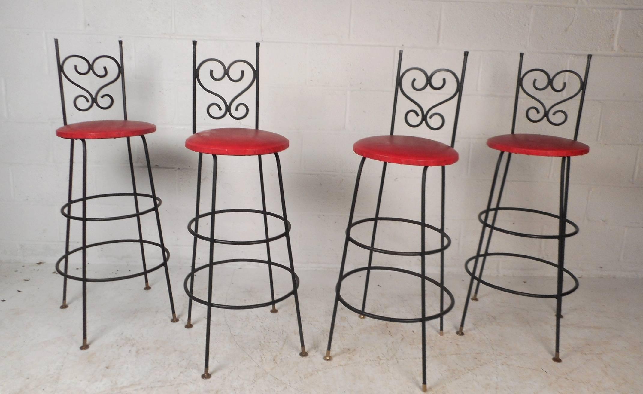 This beautiful set of four vintage bar stools feature bent wrought iron frames with vinyl covered seats. Stylish design with a thick padded seats covered in red vinyl. Unusual sculpted backrest with scroll detail and a base with two circular feet