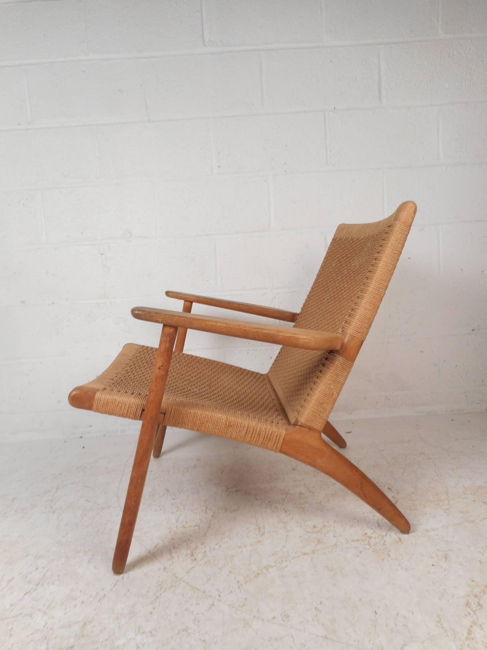 This beautiful Danish modern lounge chair features a solid oak frame with angled back legs and sculpted arm rests. Sleek design with a soft rush seat and back rest adding to the midcentury appeal. Sturdy construction with beautiful light colored