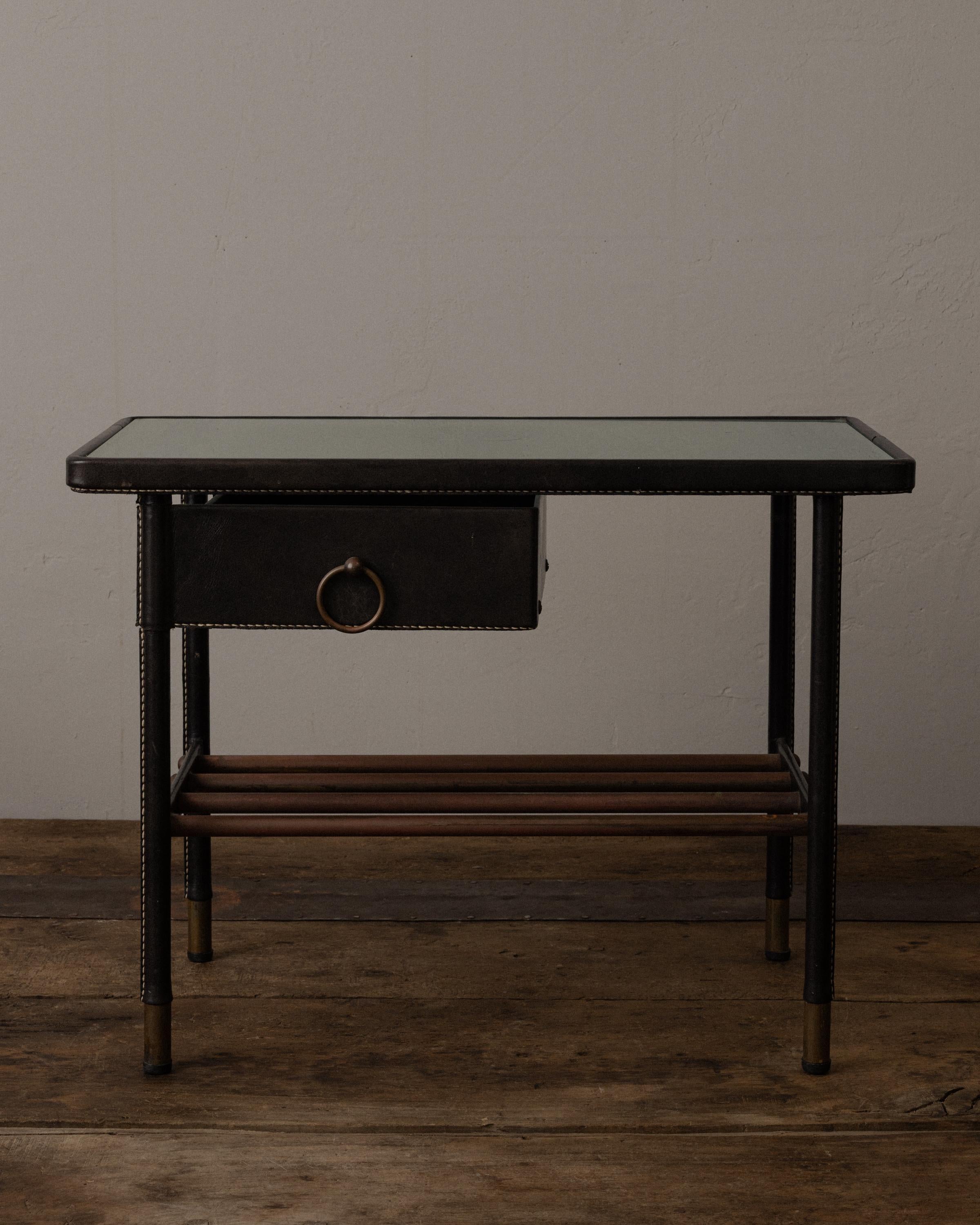 Paire de tables d'appoint raffinées du milieu du siècle par Jacques Adnet, fabriquées en France dans les années 1950. Chaque table est dotée d'un cadre en cuir noir cousu à la main, d'une piqûre sellier contrastée et d'accents en laiton patiné. Les
