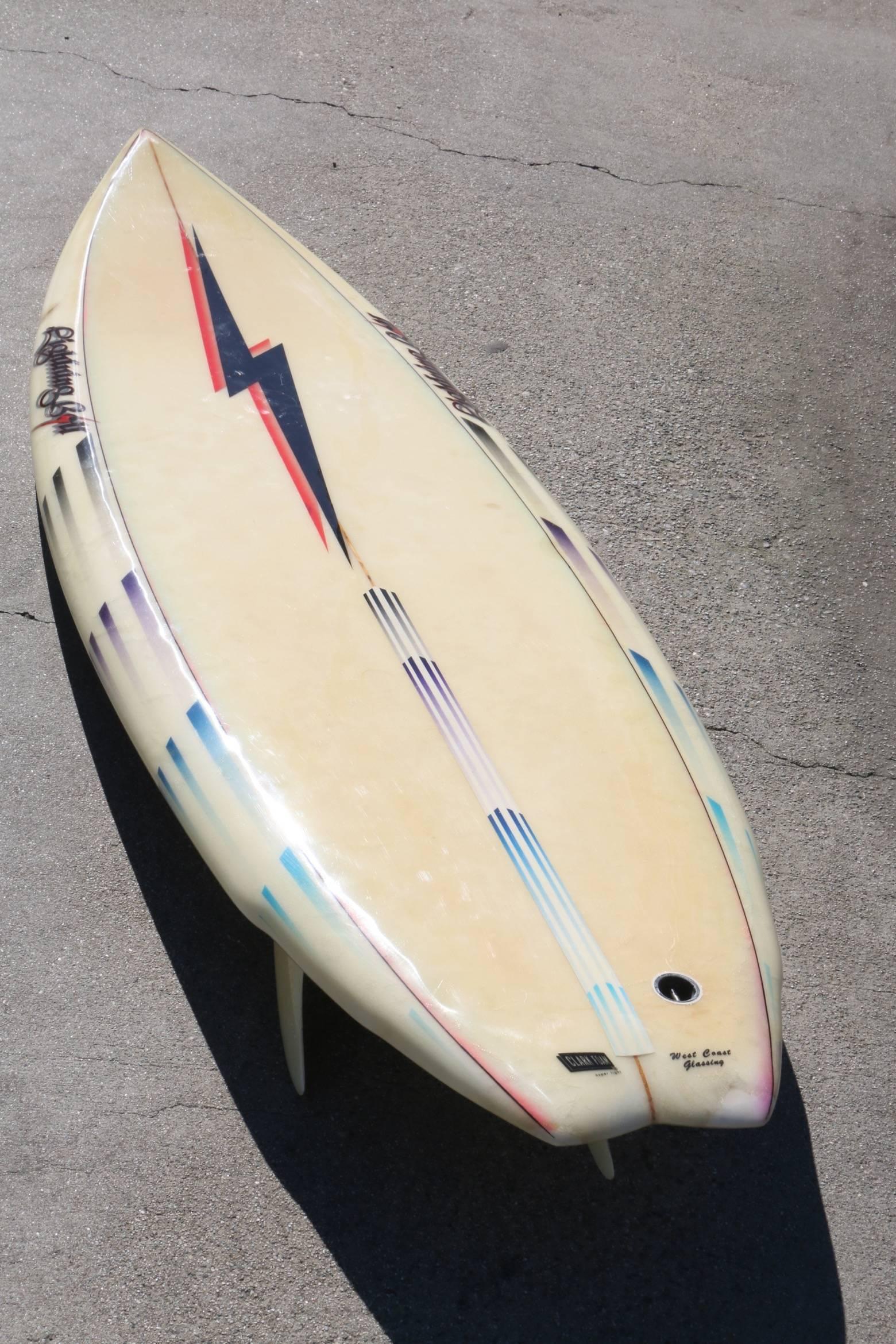 This lightning bolt surfboard with Black and Red Bolt has four lightning bolt logos, as well as one Clark Foam and one West Coast Glassing logo. Made in the 1980s it is a double wing swallow tail design and has three fins with the centre fin