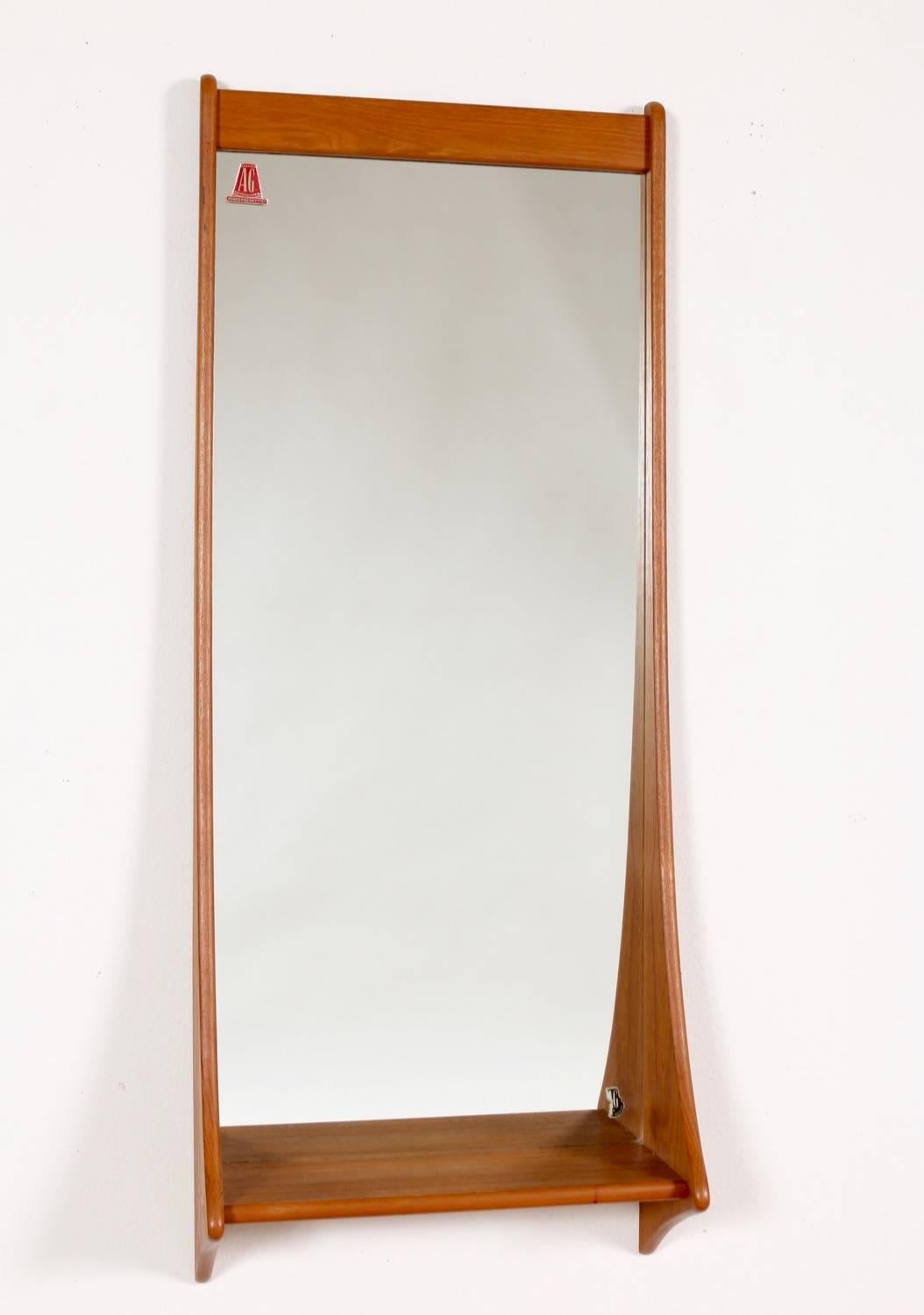 This sculptural teak, hanging wall mirror with shelf by Pedersen and Hansen, offers impactful artistic style and function in a relatively narrow space. Measuring 43.5 inches high x 17.5 inches wide x 6.6 inches deep the shelf is deep enough to hold