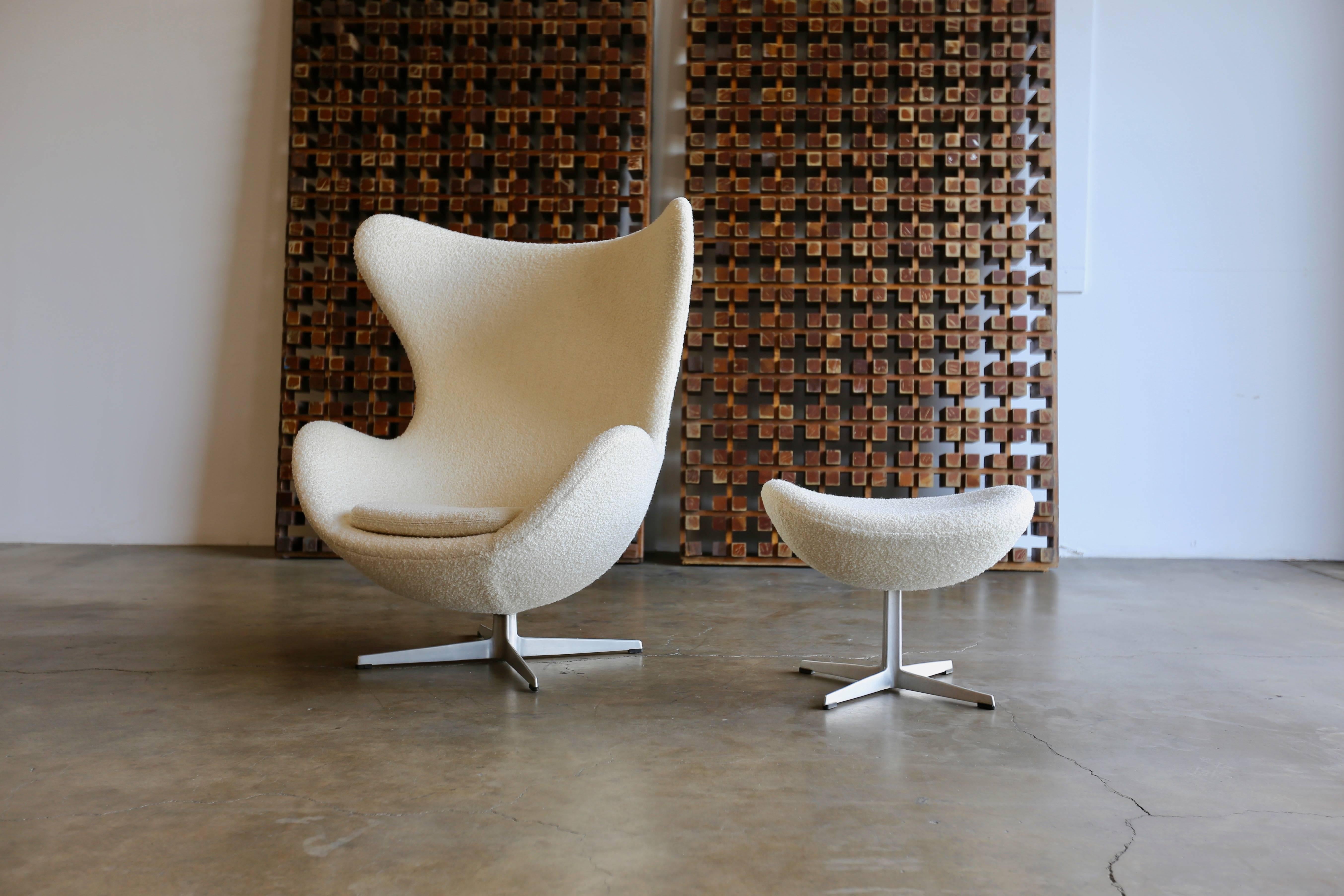 Egg chair and ottoman by Arne Jacobsen for Fritz Hansen. This chair and ottoman has been upholstered in a nubby cream colored boucle. The chair retains the original Fritz Hansen label to the base.