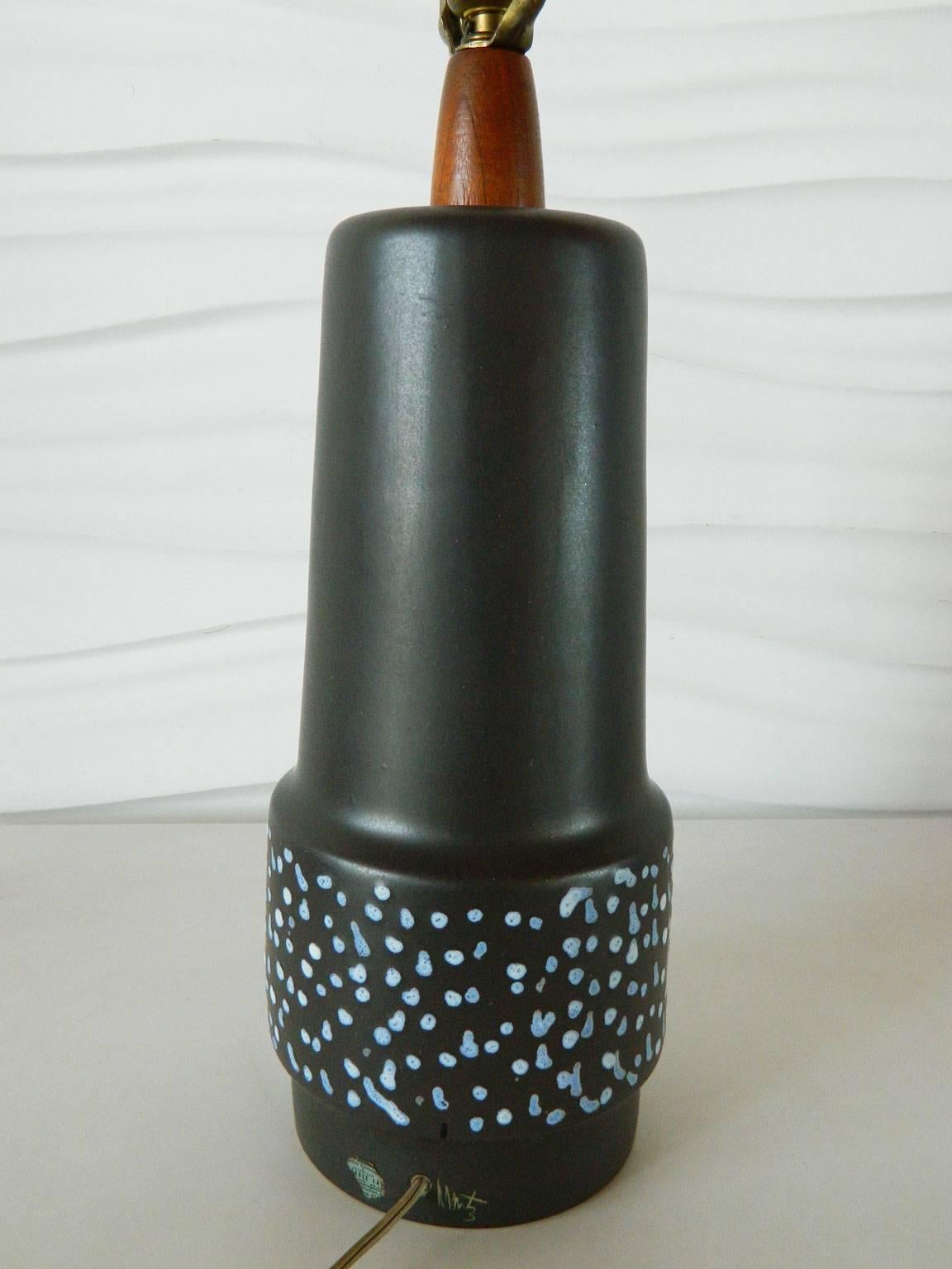 Designed by artists Gordon and Jane Martz in the 1960s, this matte black ceramic lamp features a walnut neck and painted blue and white decoration. Measures 18 inches tall to the top of the wooden neck.
