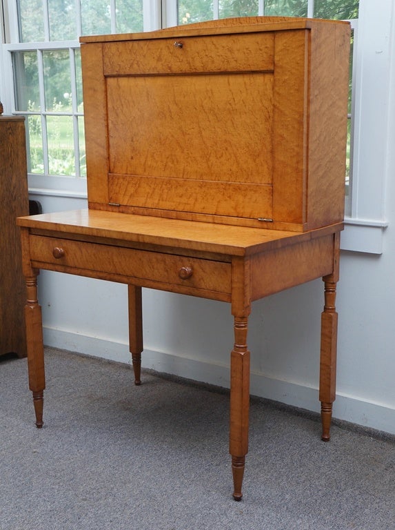 A birdseye maple one drawer drop front desk. The drop down reveals  an interior with three cubbies, three file slots and an enclosed drawer. The New York style legs are turned in tiger maple. This 1860 desk is constructed of solid birdseye maple and