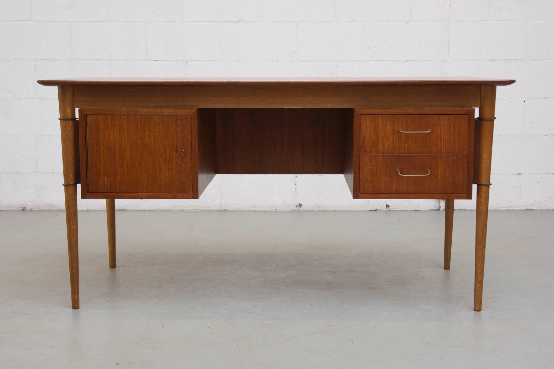 Executive desk in teak with two small side cabinets, one with a door and sliding tray. The other with two side stacking drawers and brass pulls. Beautiful brass ring detail around the legs.