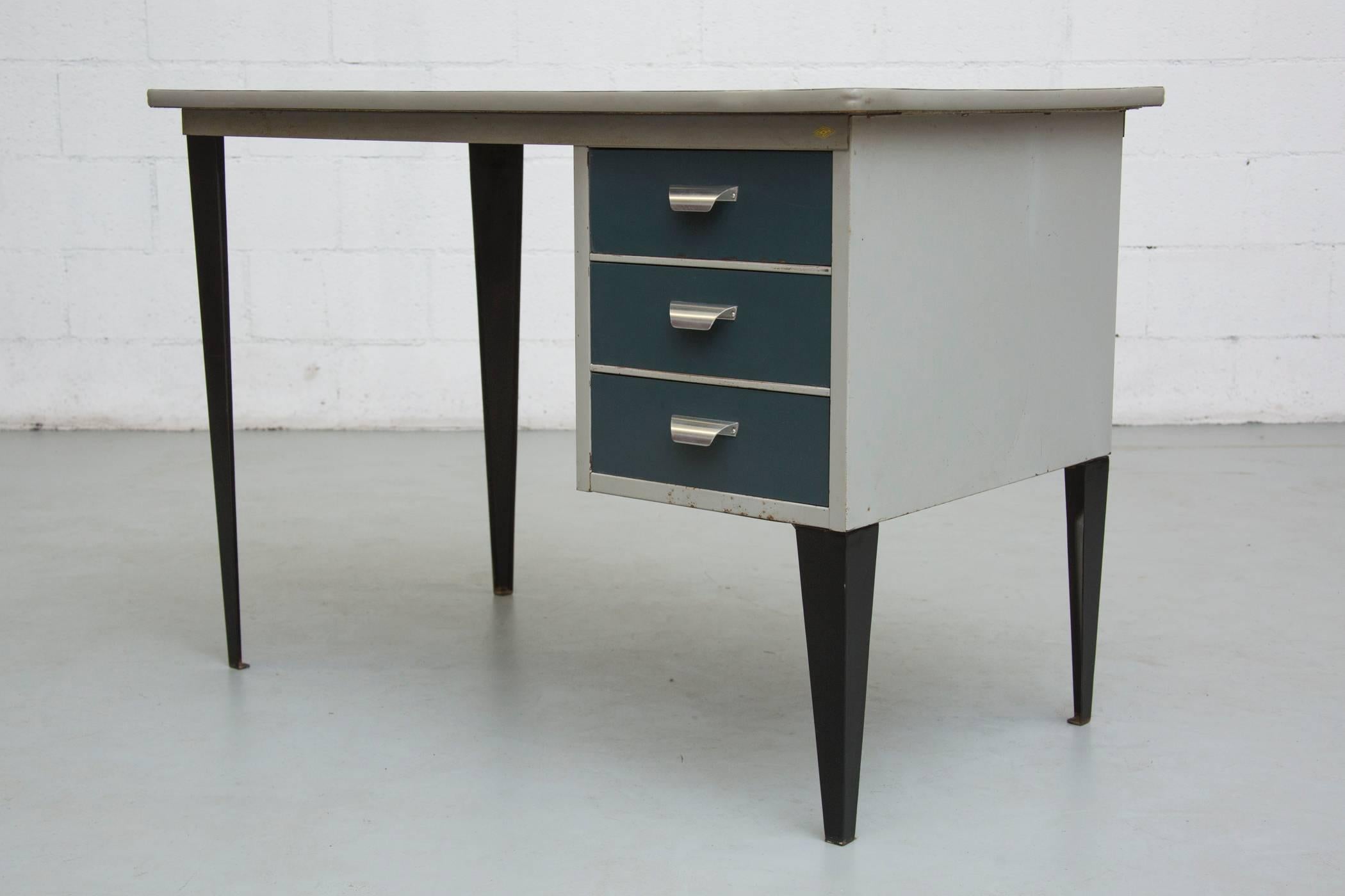 Elegant little metal enameled desk with linoleum top, grey body with Mediterranean blue drawers and black enameled metal legs. In original condition with visible signs of wear.