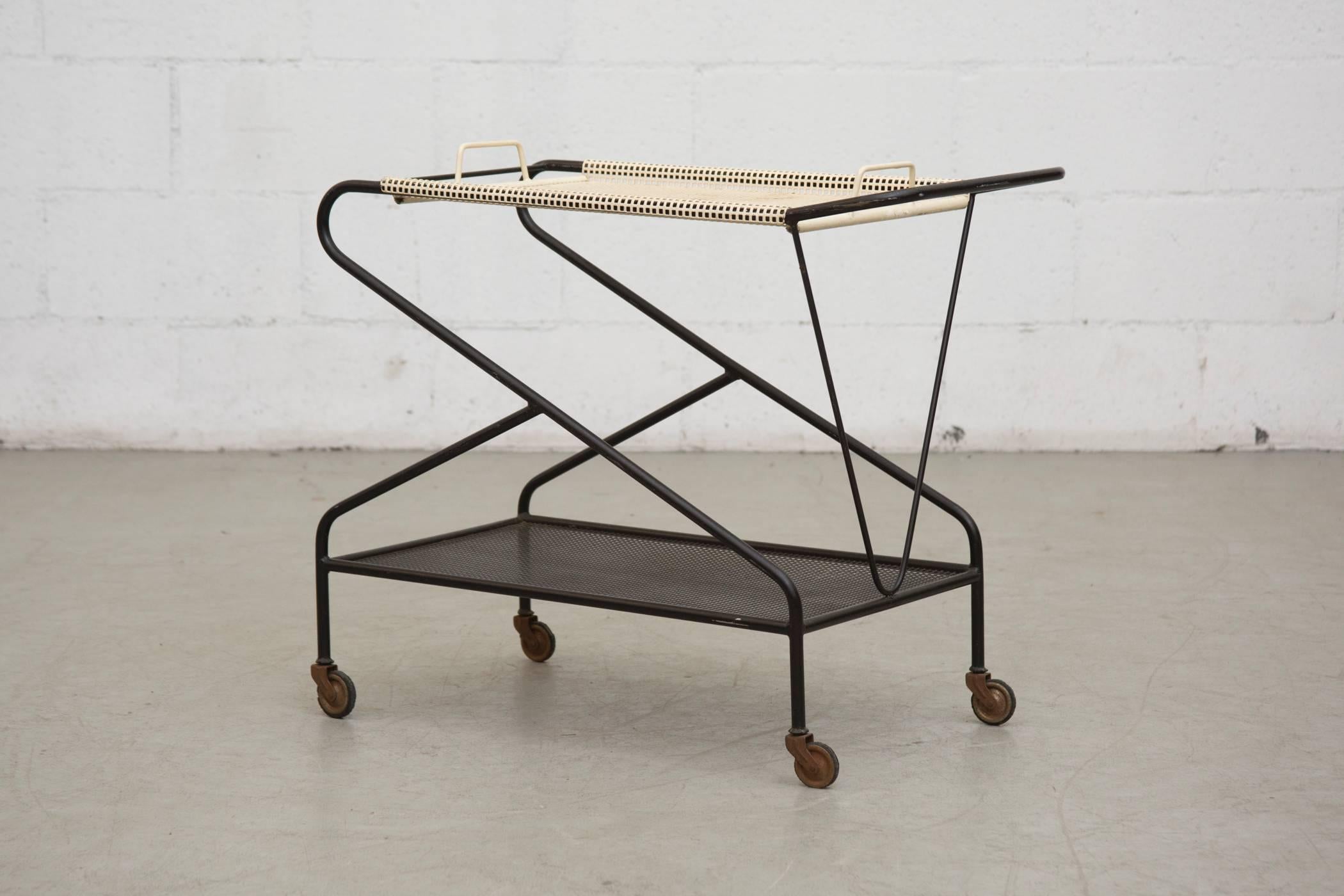Utterly cool Mathieu Mategot inspired, rare Pilastro rolling cart with perforated shelves. Top shelf is a removable handled tray. Visible wear and some enamel loss with slight signs of surface rust. Wheels have heavy surface rust as well. In